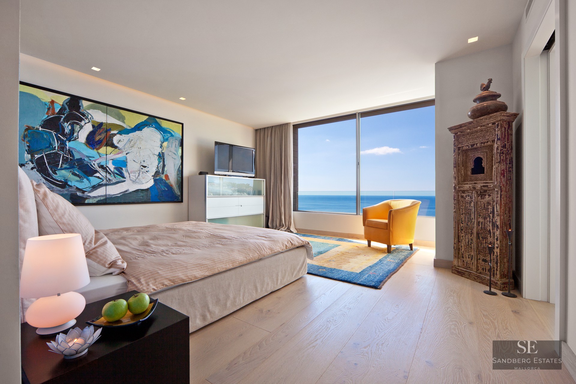 Modern master bedroom featuring floor-to-ceiling sea views, a yellow armchair, and eclectic art.