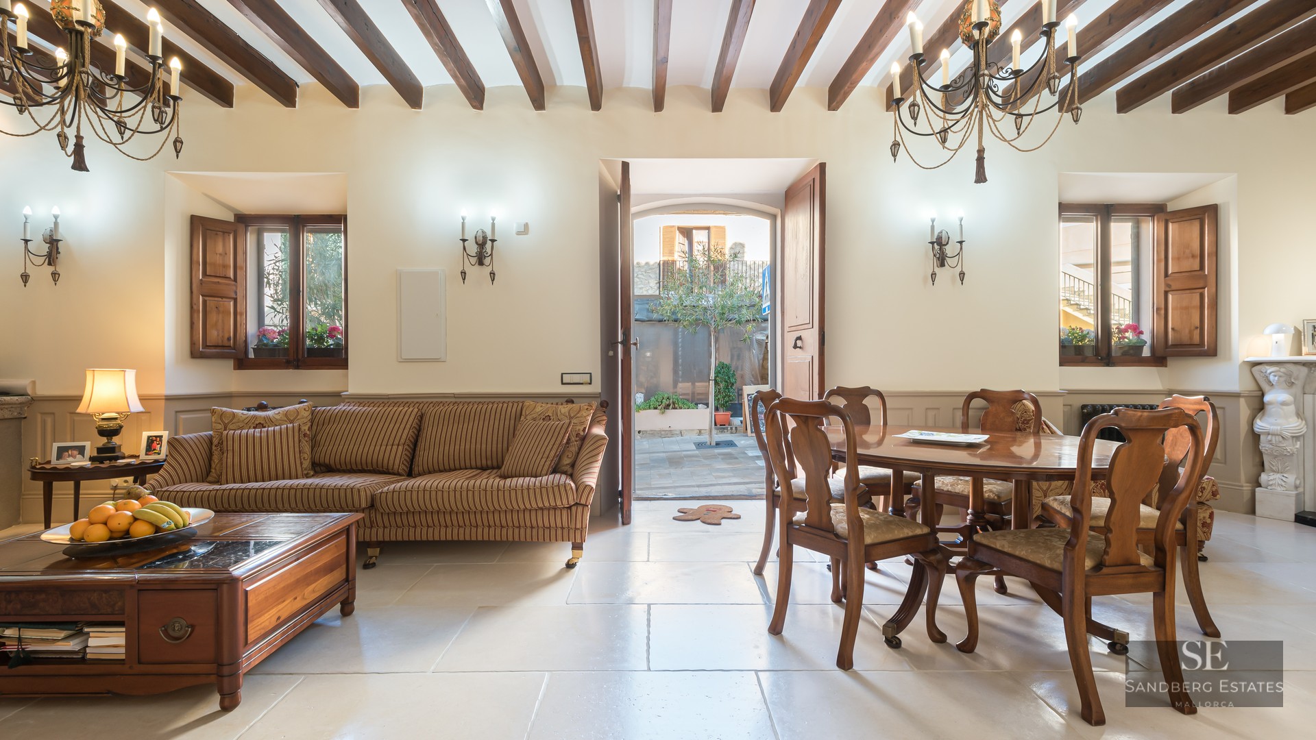 Rustic interior with a striped sofa, wooden dining table, stone floors, and exposed wooden ceiling beams.