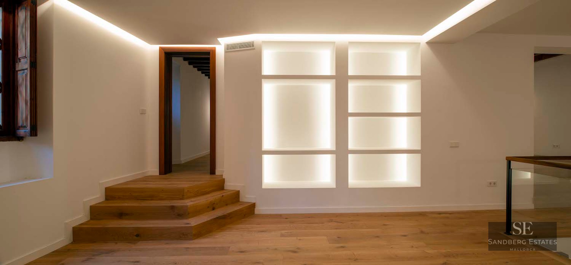 Modern room with wood floors, oak steps, and built-in shelving illuminated with warm LED lights.