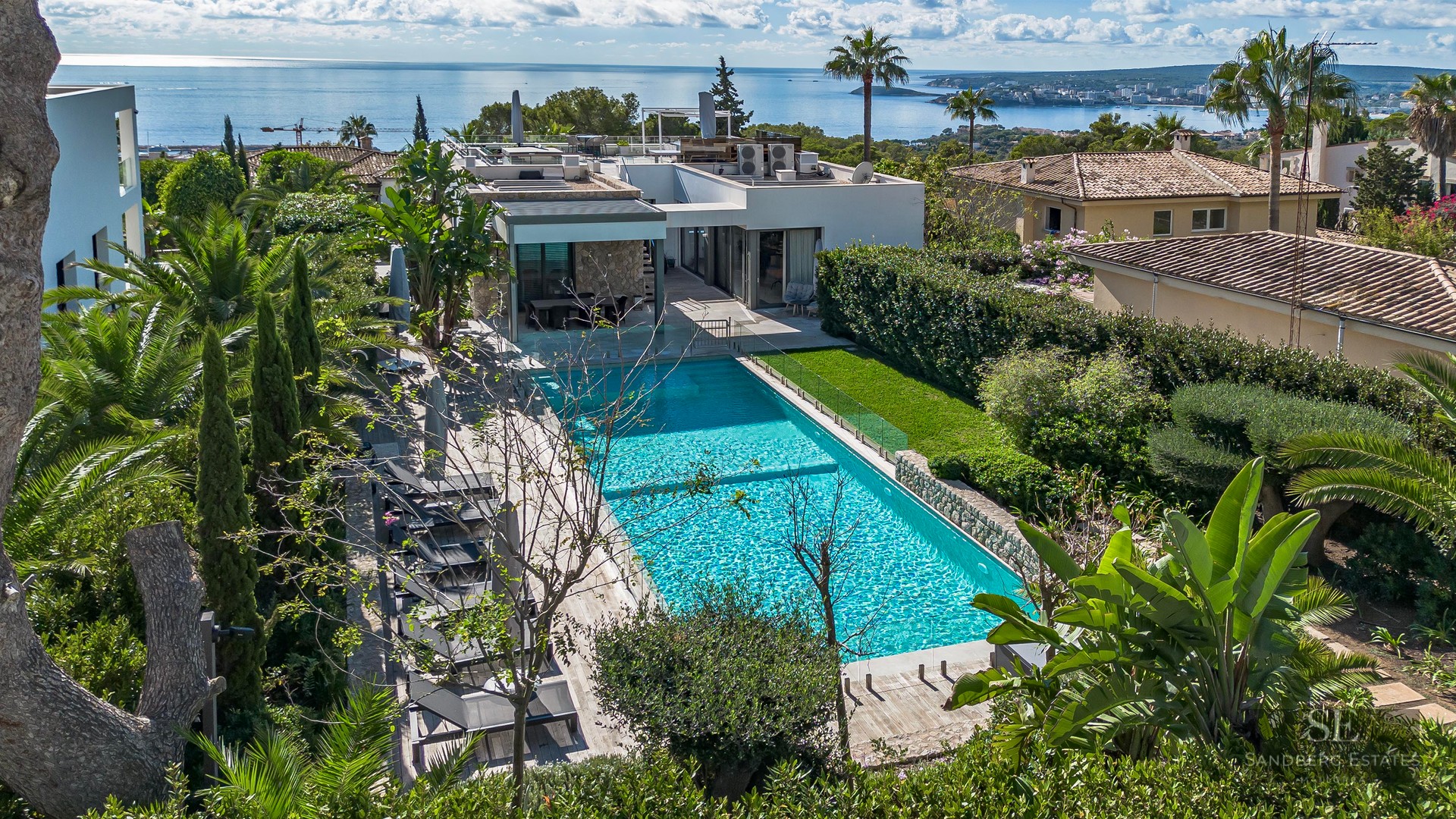 Grande piscine turquoise entourée d'un jardin luxuriant et d'une terrasse en bois avec vue panoramique sur la mer Méditerranée.