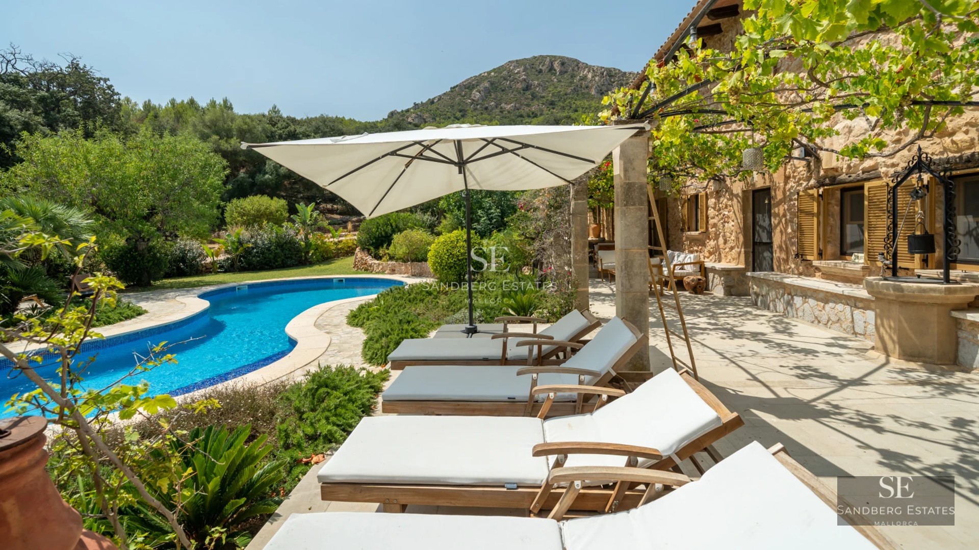 View of a modern villa's pool with outdoor seating area, lounge chairs, and lush gardens. Minimalist architecture with large windows.