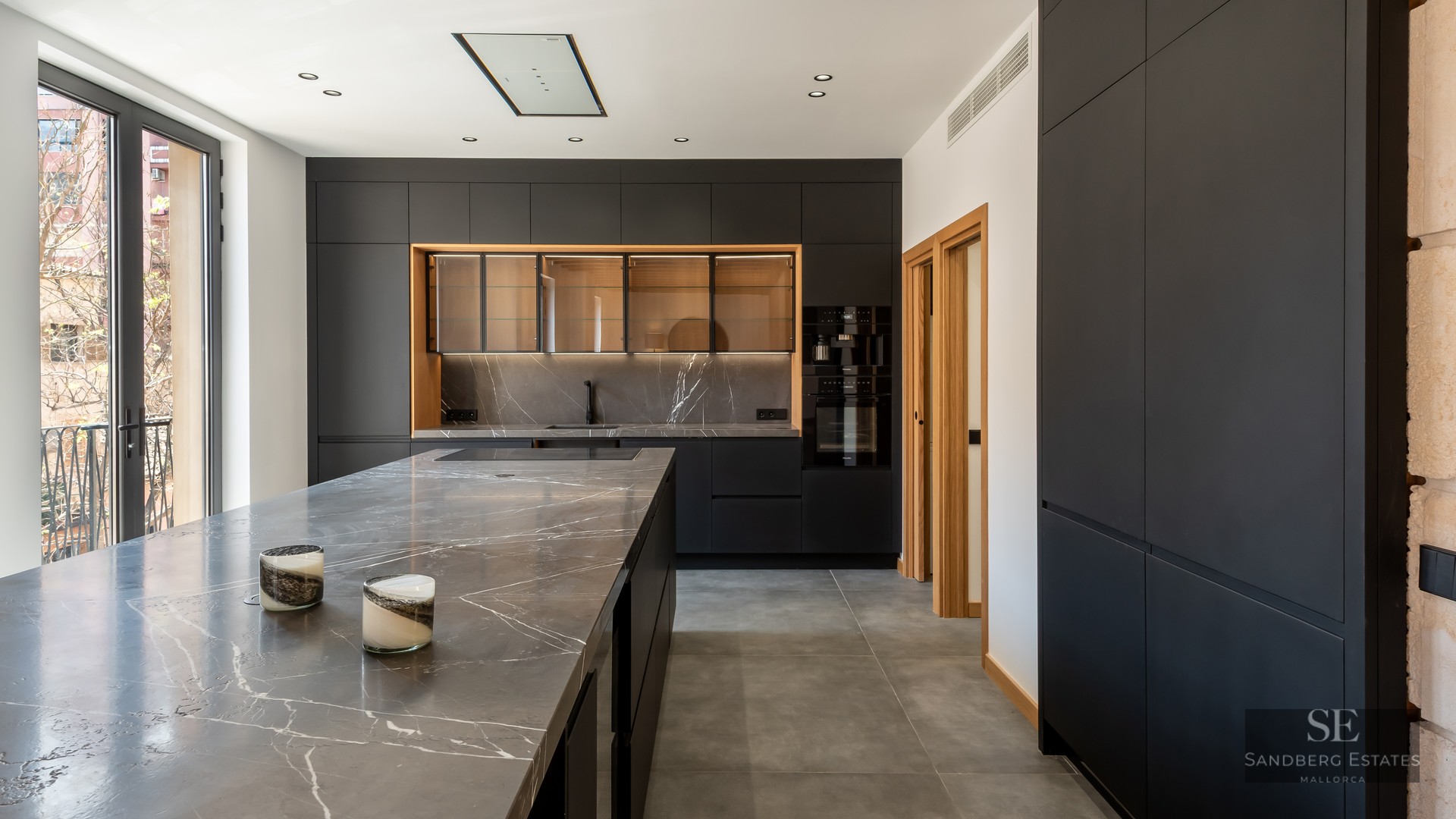 Modern kitchen featuring matte black cabinetry, grey veined marble countertops, and large windows.