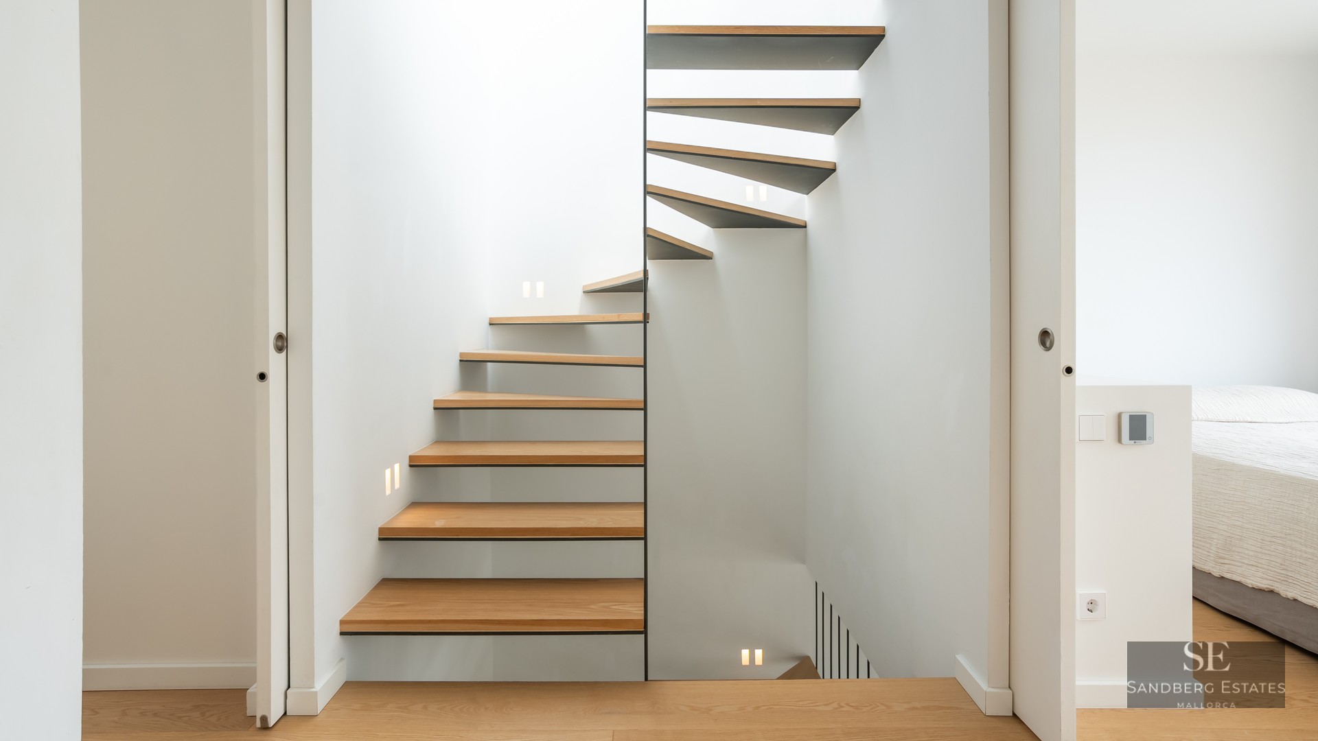 Modern spiral staircase with oak steps and white walls featuring integrated LED square lights.