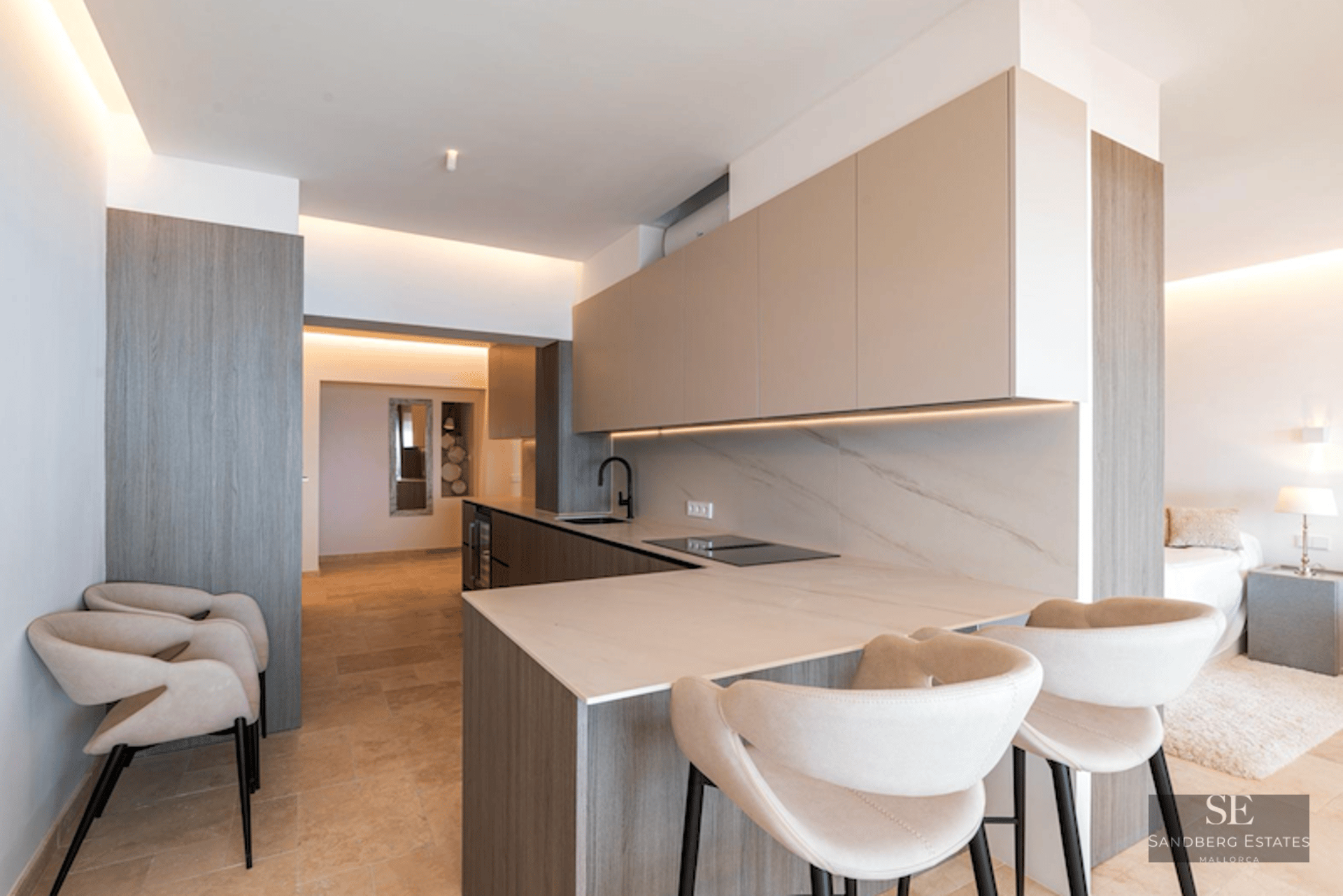 A sleek modern kitchen with light wood cabinets, stone countertops, and cream-colored designer bar stools.