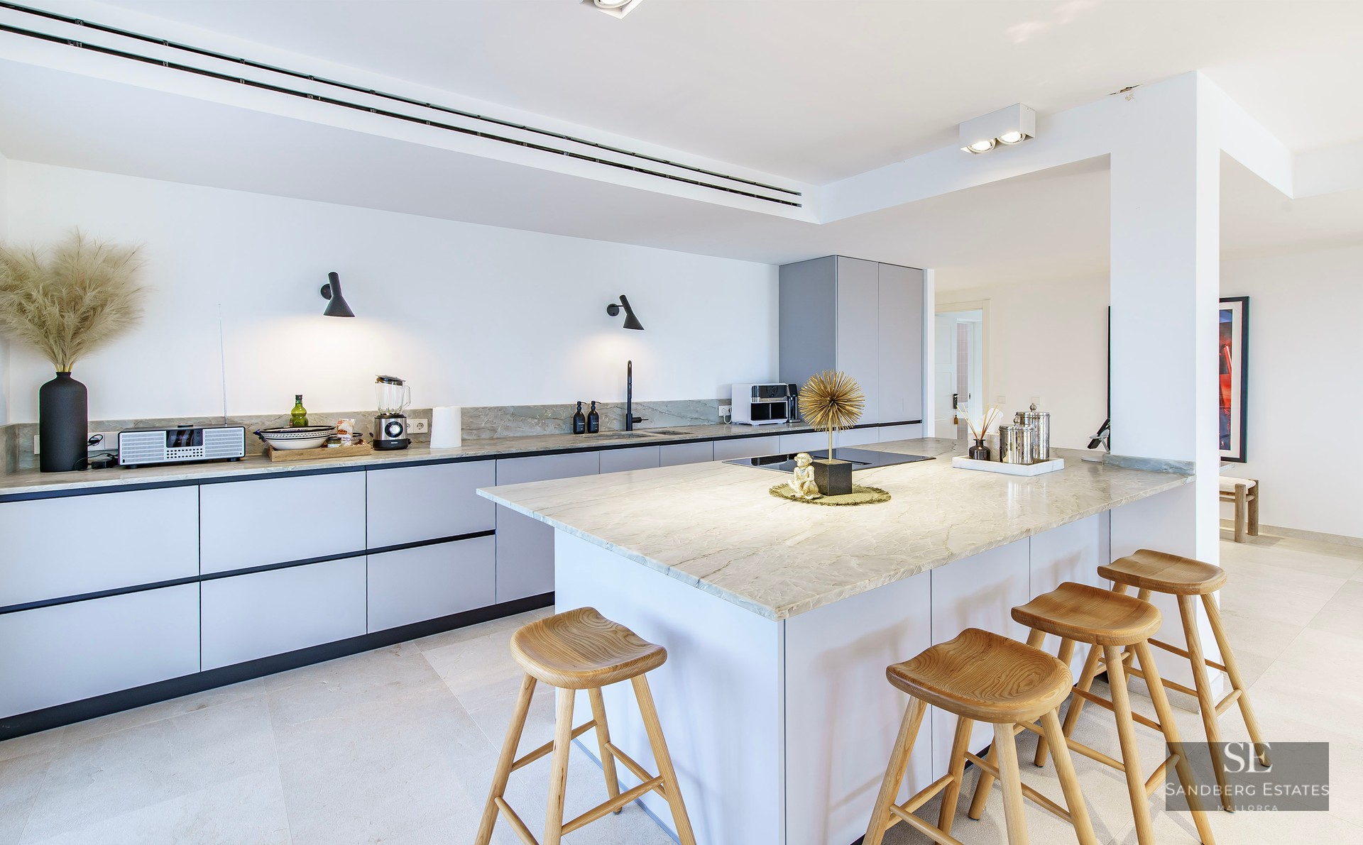 Modern kitchen featuring a large marble-topped island with four wooden stools and minimalist grey cabinetry.