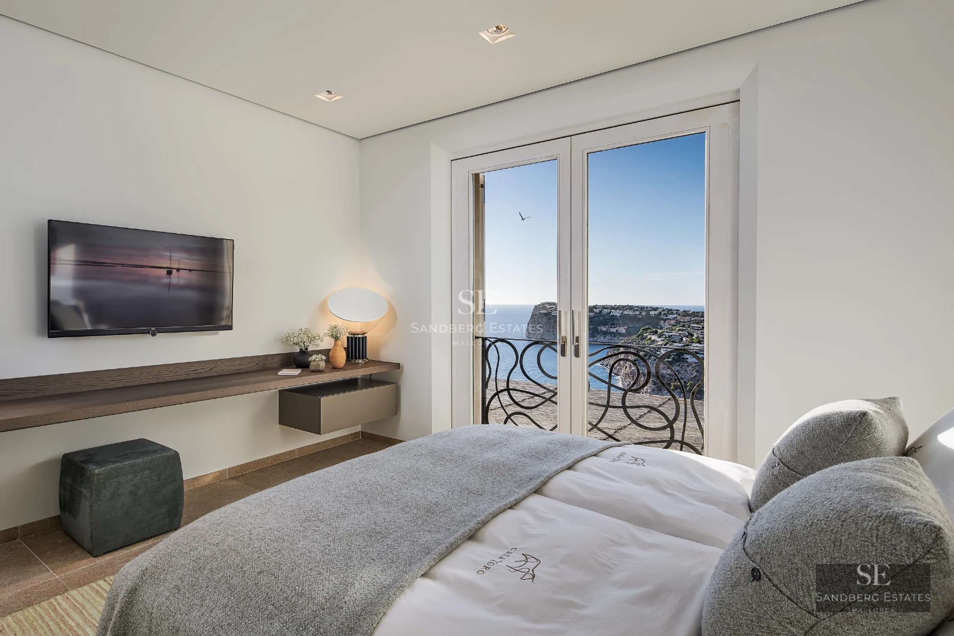 Spacious living room with window walls, beige sofa, light wood floor, designer rug, and panoramic sea view. Natural lighting.