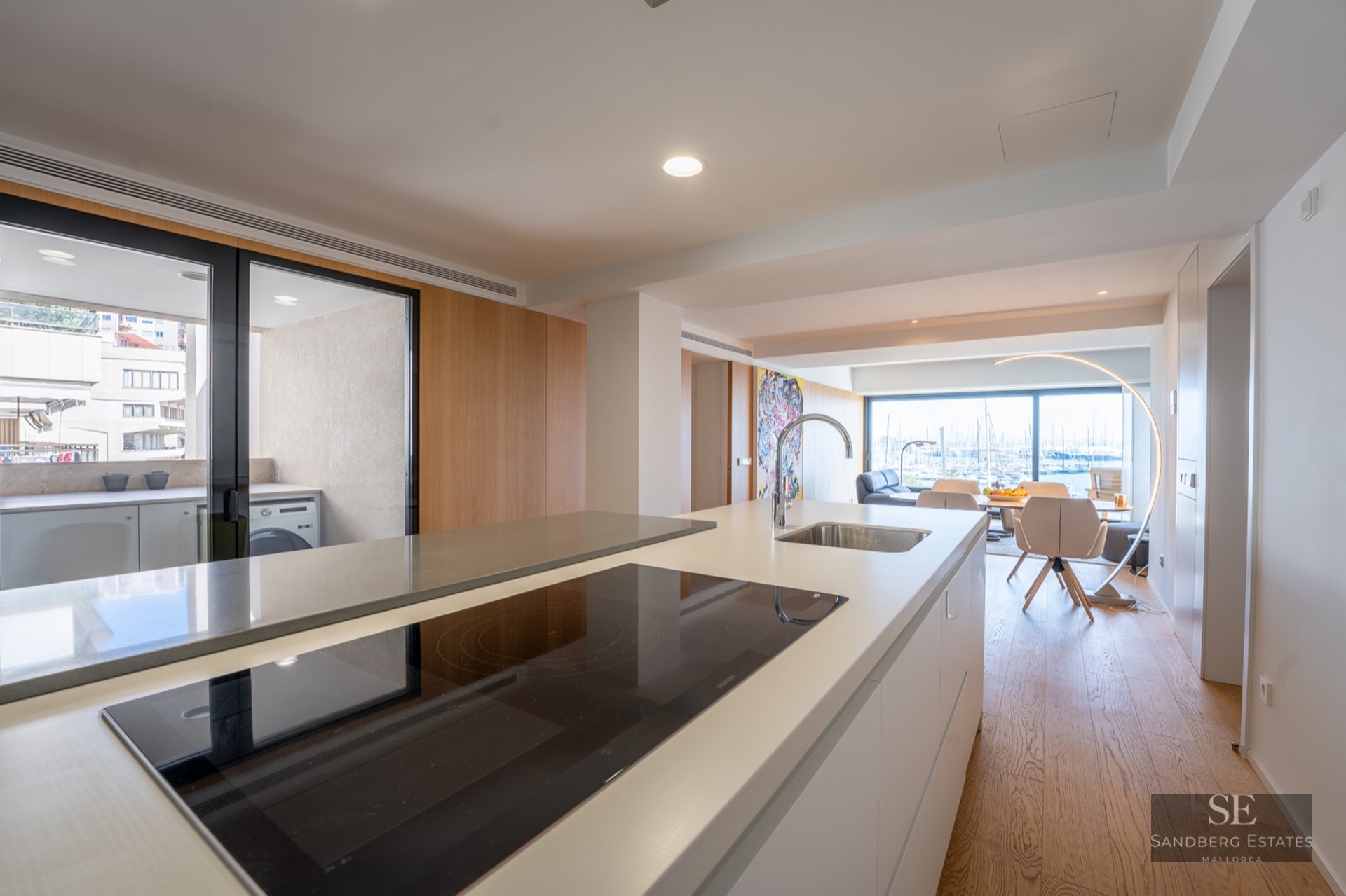 Modern white kitchen island with induction cooktop and sink, overlooking an open dining area and harbor view.