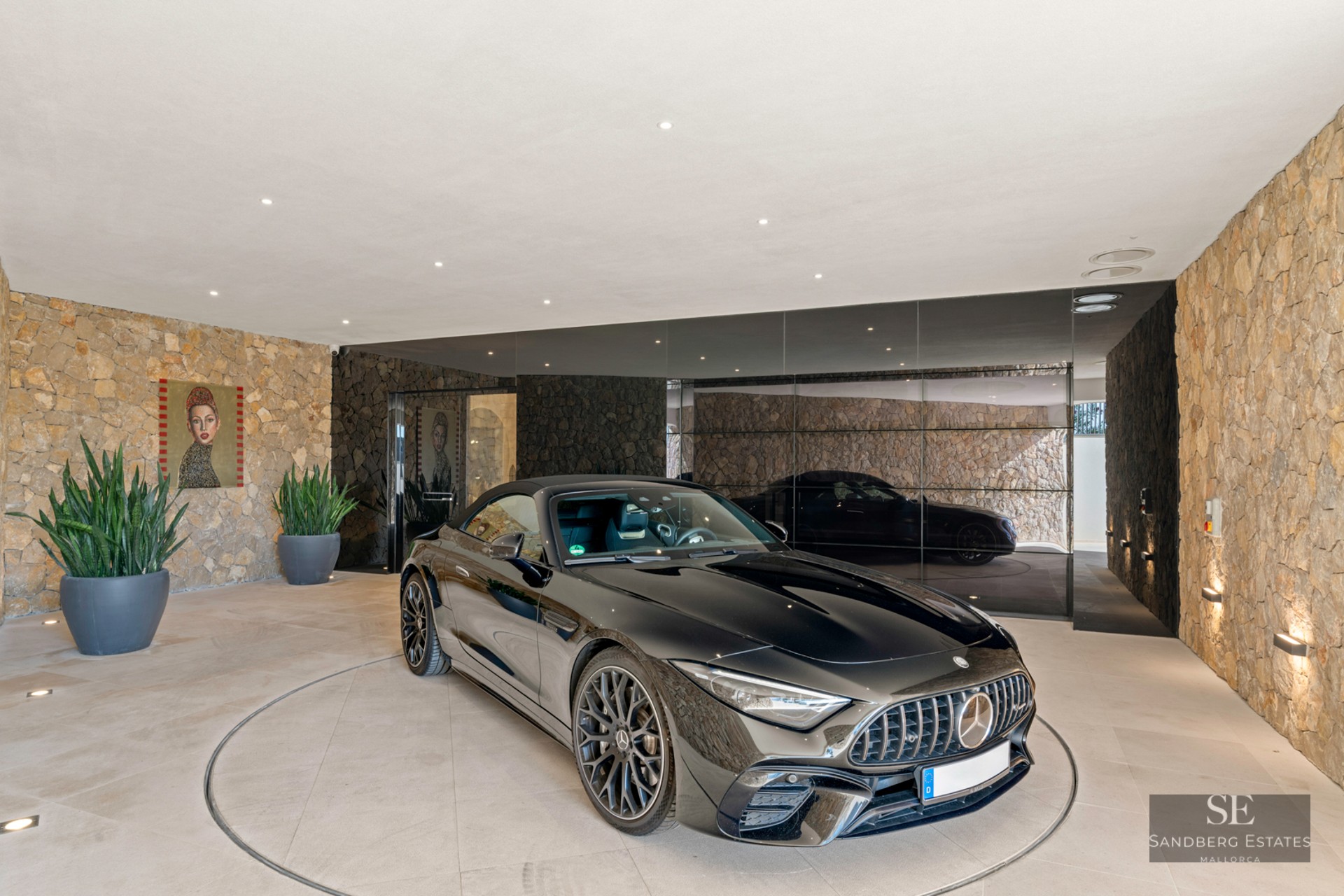 A black Mercedes sports car on a circular rotating platform in a modern garage with natural stone walls and mirrors.