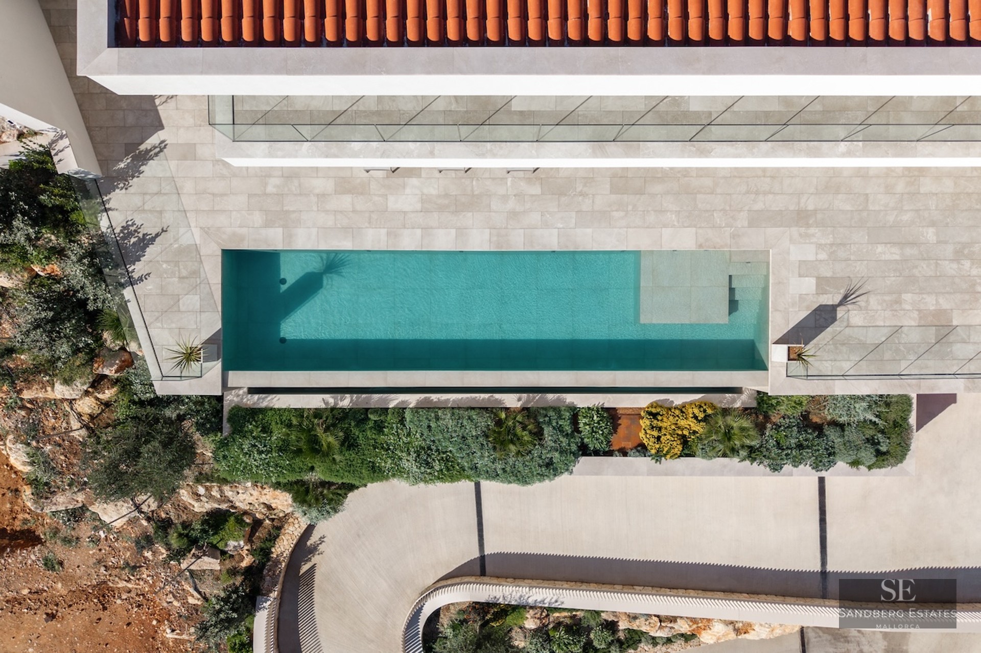 Bird's eye view of a turquoise swimming pool, stone terrace, terracotta roof, and lush Mediterranean landscaping.
