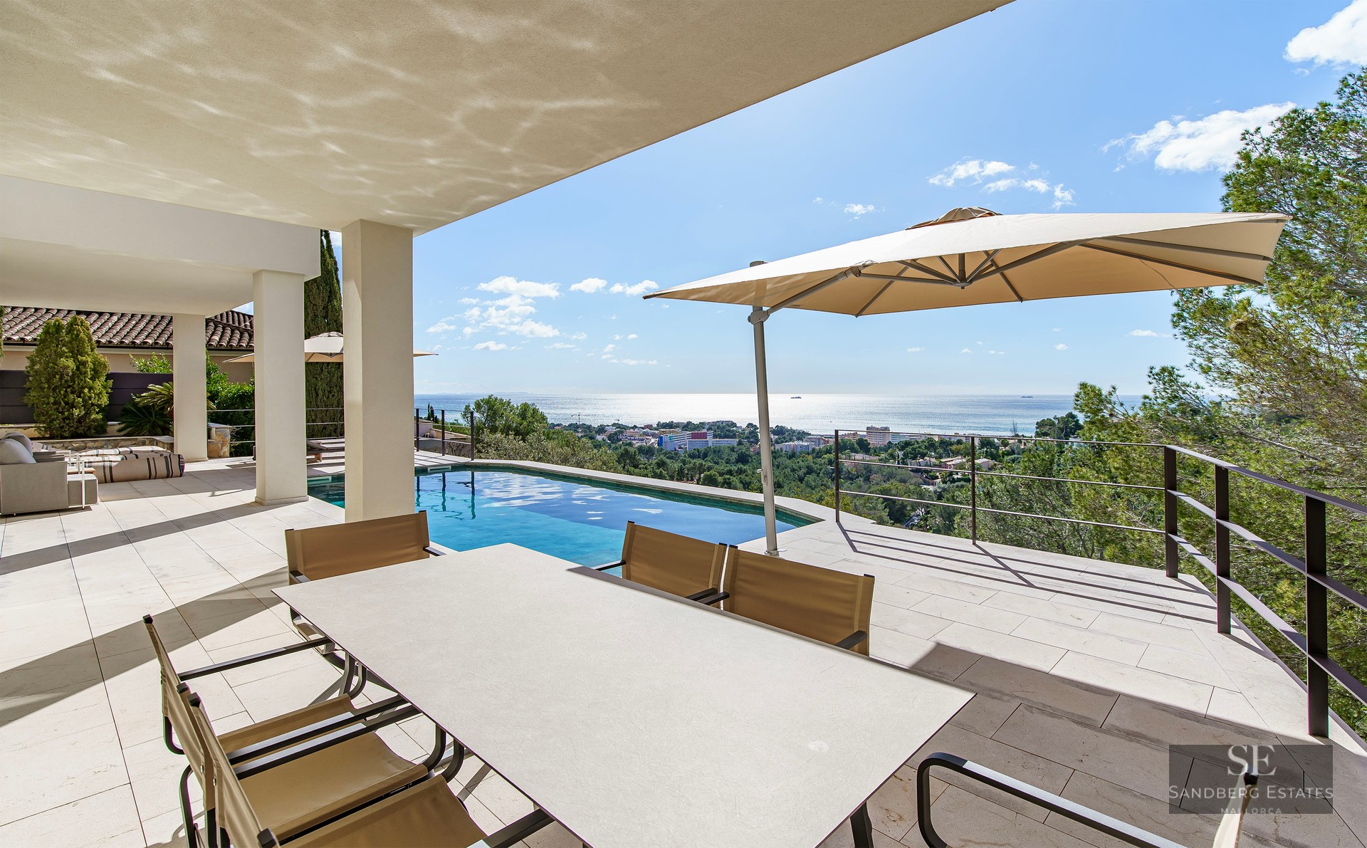 Spacious modern terrace with an infinity pool, dining area, and panoramic sea views under a clear blue sky.