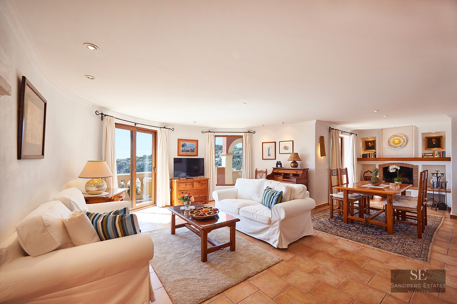Spacious living room with white sofas, terracotta floors, a fireplace, and a dining area with wooden furniture.