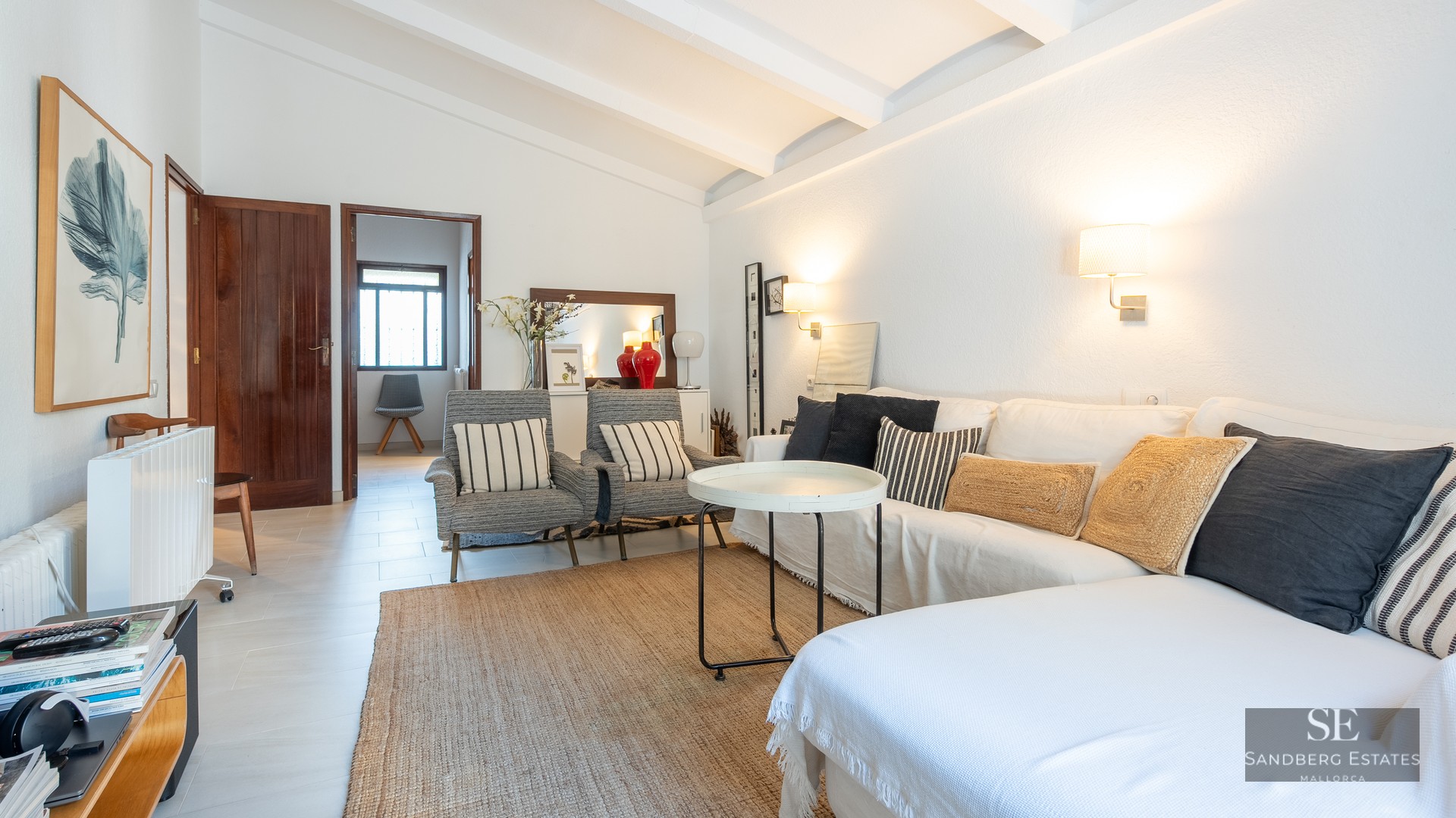 Bright living room featuring a white sofa, striped armchairs, a jute rug, and white exposed ceiling beams.
