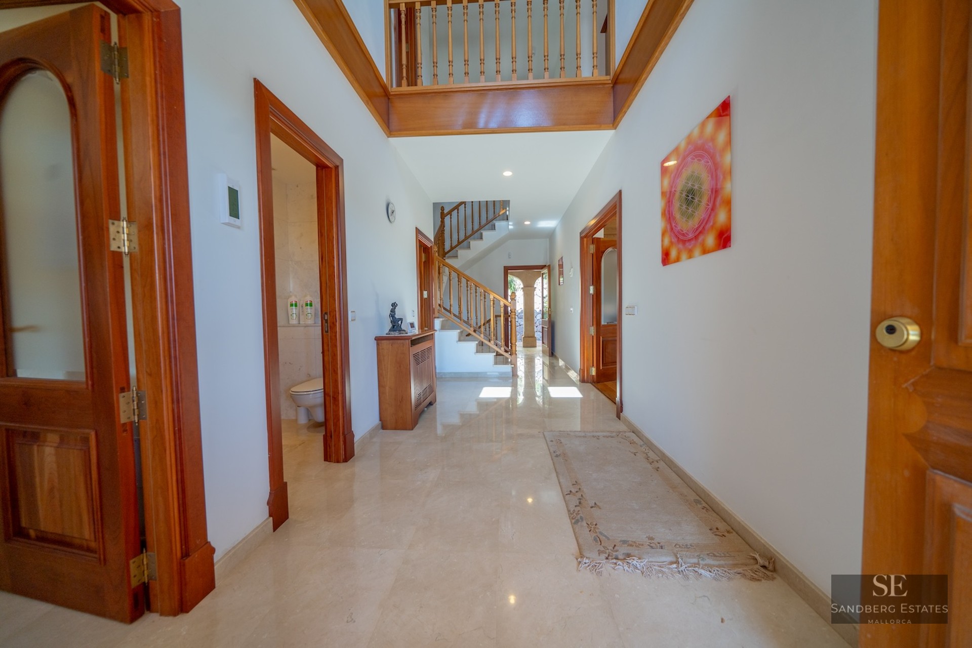 A bright hallway with polished marble floors, wooden doors, and a staircase leading to the upper floor.
