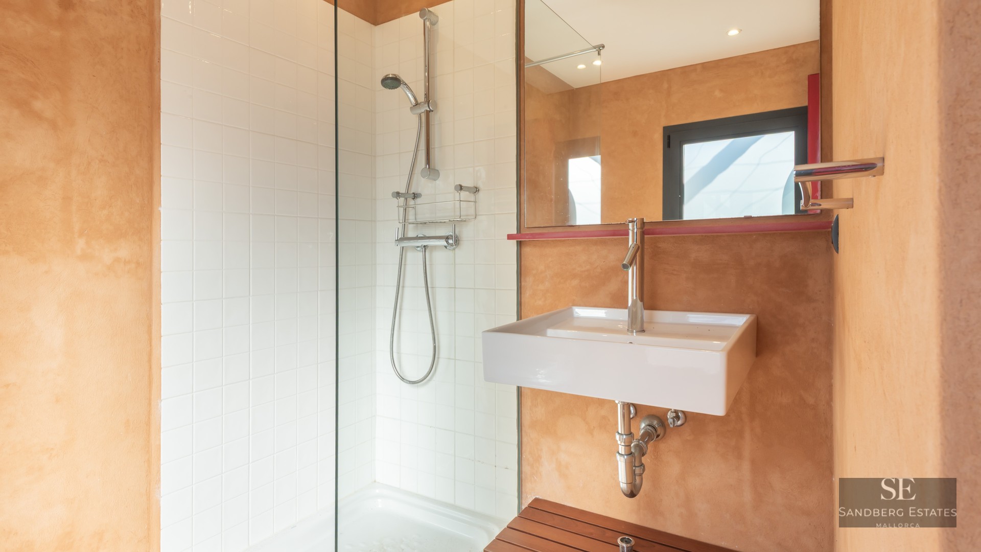 Modern bathroom featuring a walk-in glass shower, white square tiles, and warm terracotta textured walls with a white sink.