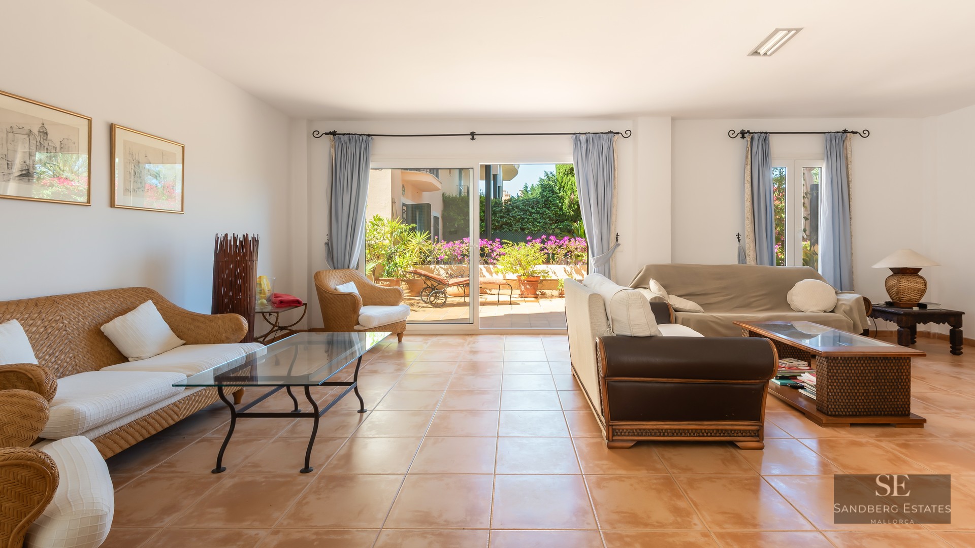Spacious living room featuring wicker sofas, terracotta tiling, and large sliding glass doors opening to a sunny terrace.