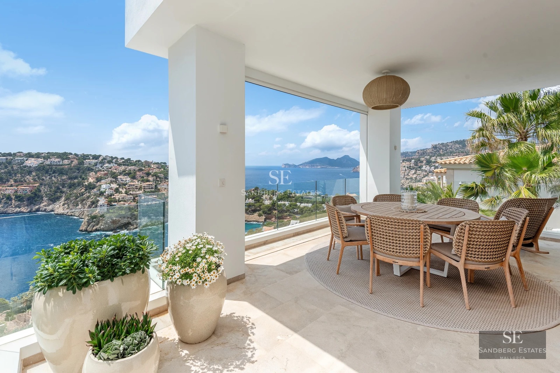 Spacious balcony with sea view. Glass railing, modern furniture, and light wood flooring. Relaxing and bright atmosphere.