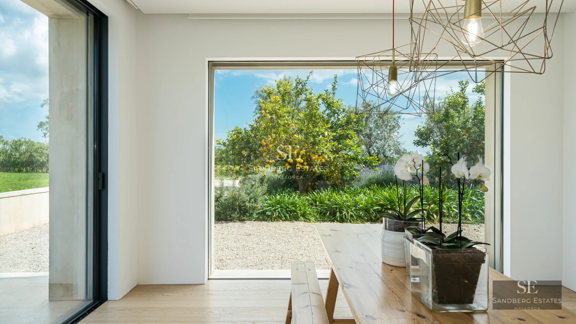 Modern living room with large windows, light wood flooring, grey sofas, and panoramic sea views. Abundant natural lighting.