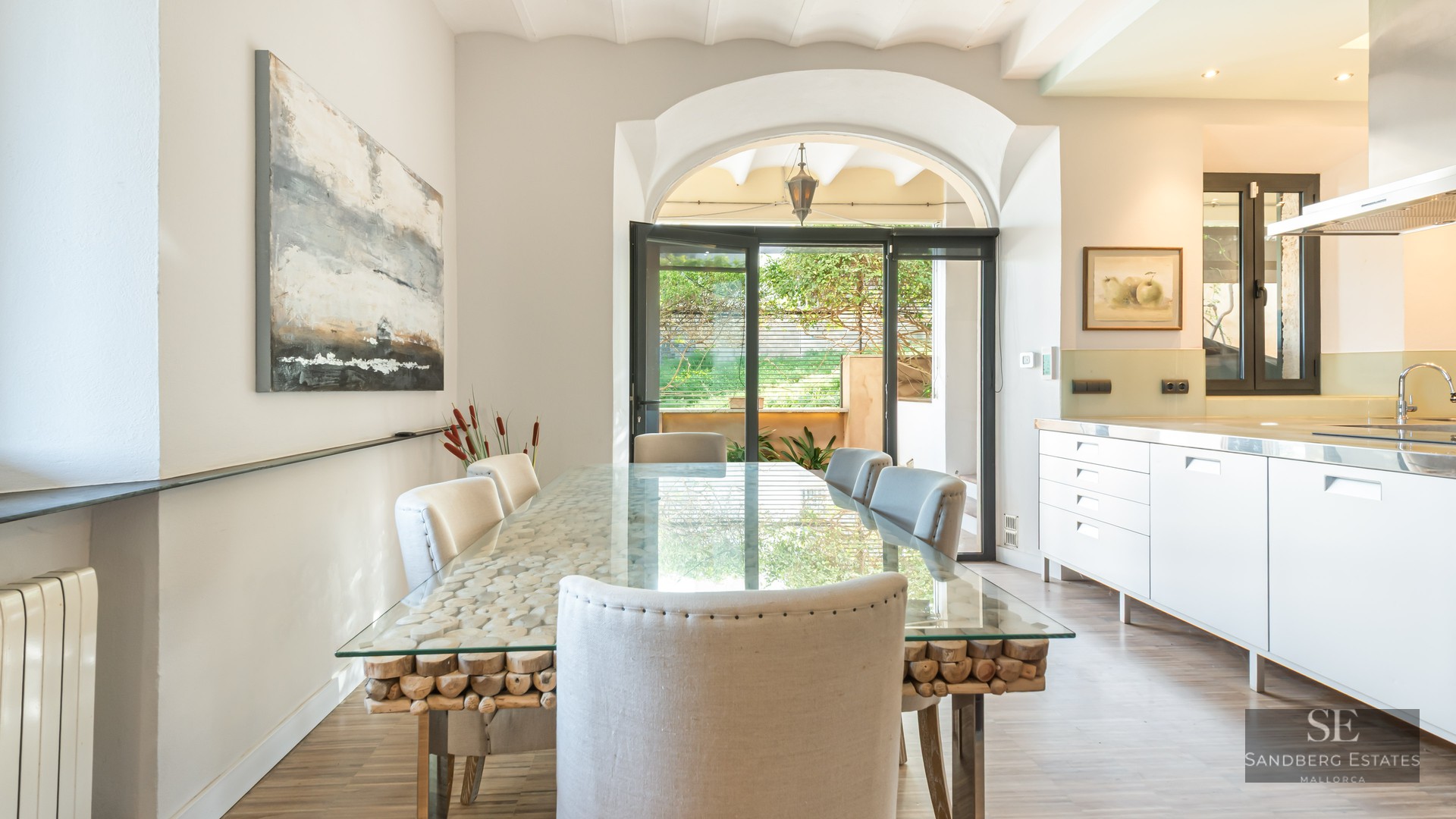 Bright dining room featuring a glass-top table with a rustic wood log base, white upholstered chairs, and an archway.