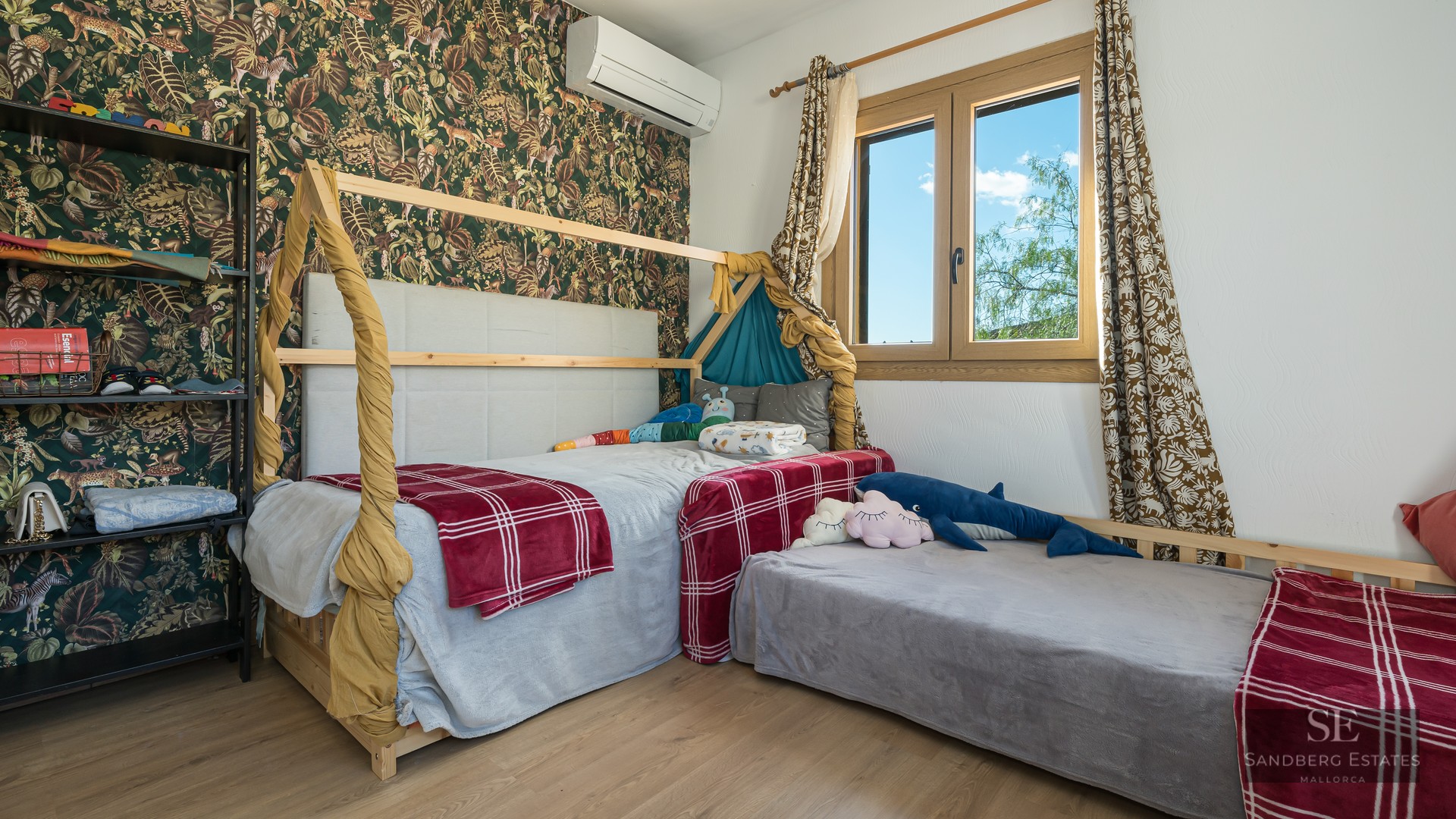 Bright child's bedroom featuring a wooden house bed, jungle wallpaper, and natural light.