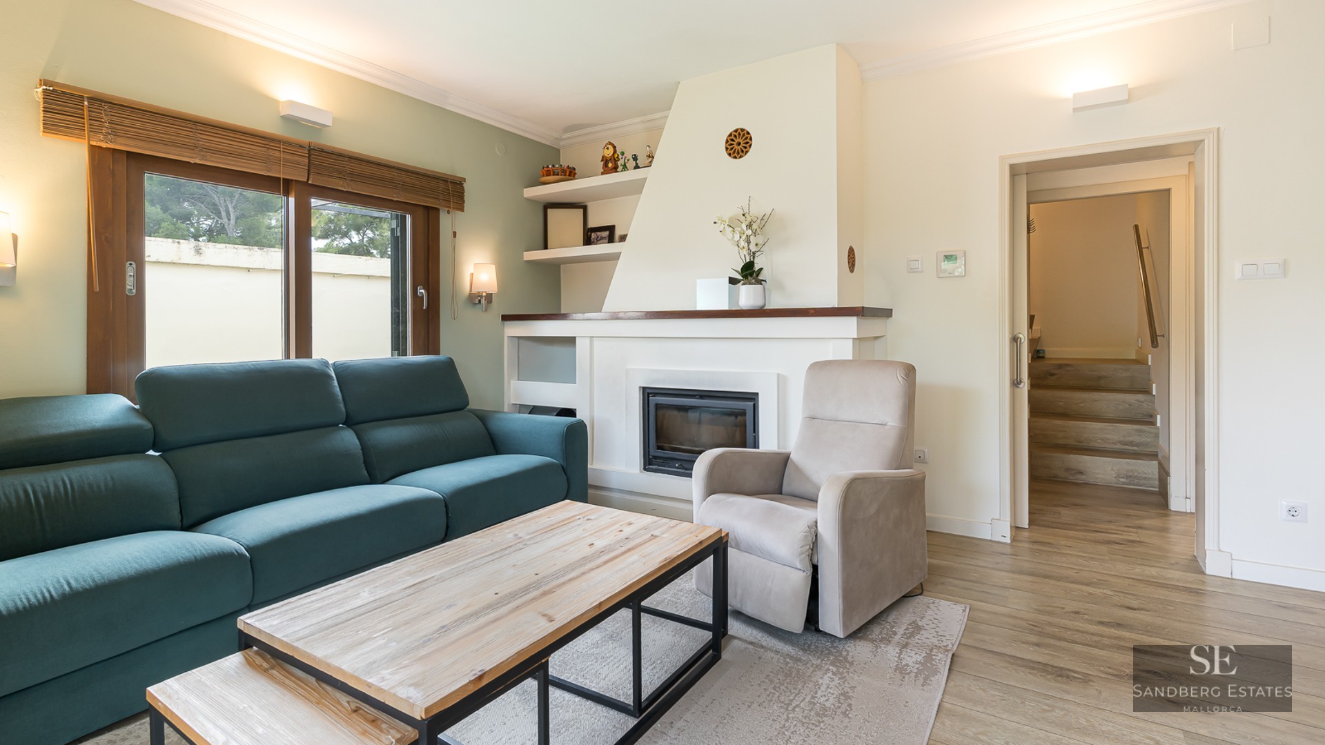 Modern living room with a teal sofa, white built-in fireplace, wooden coffee table, and beige armchair.