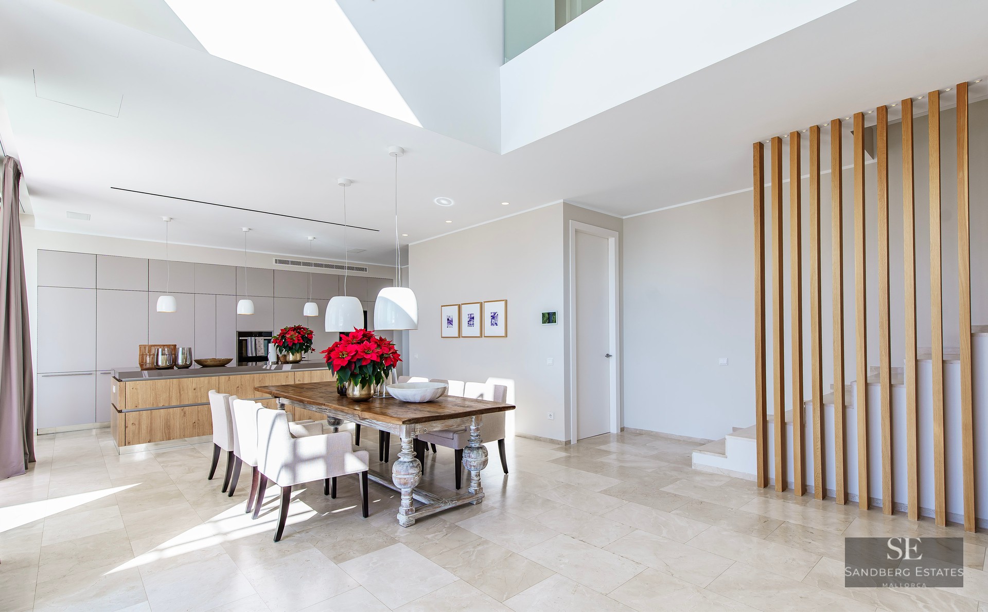 Bright open-concept dining room with a rustic wood table, marble floors, and a modern wooden slat staircase partition.