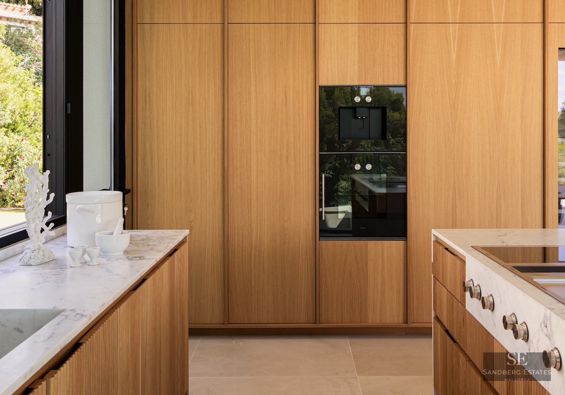 Modern kitchen featuring floor-to-ceiling oak cabinets, white marble countertops, and integrated black appliances.
