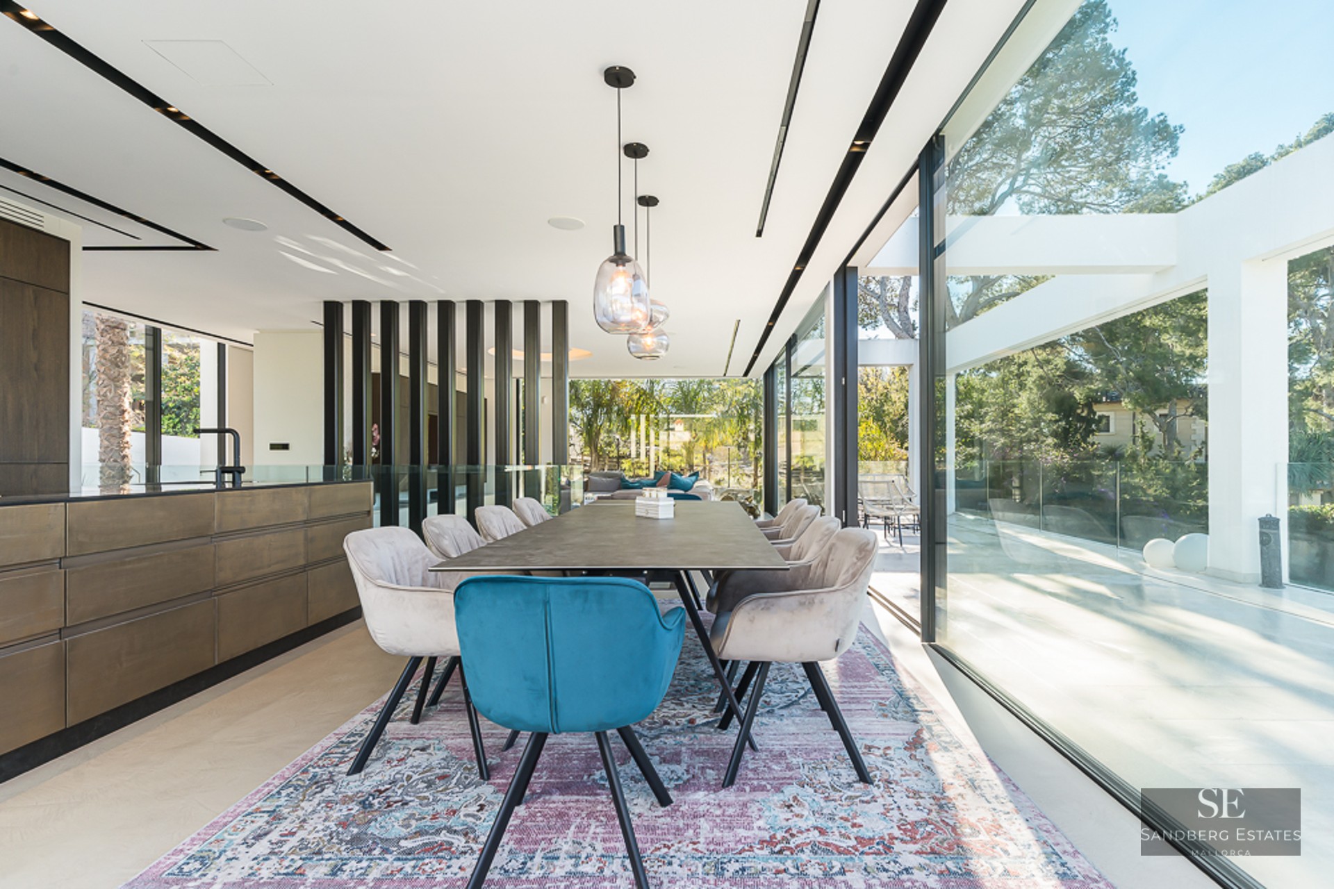Bright dining room featuring a designer table, blue and beige velvet chairs, and floor-to-ceiling glass walls.