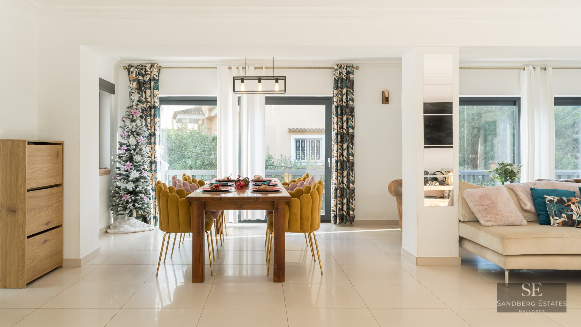 Espace salle à manger moderne avec table en bois, chaises en velours jaune, sapin de Noël et grandes baies vitrées.