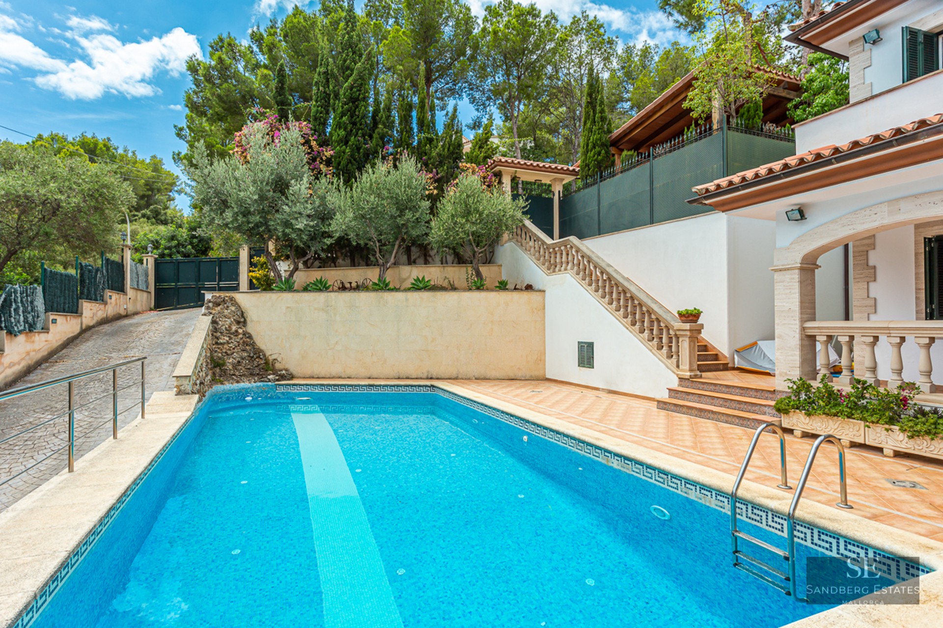 Rectangular blue swimming pool with stone stairs, surrounded by lush greenery and Mediterranean architecture.