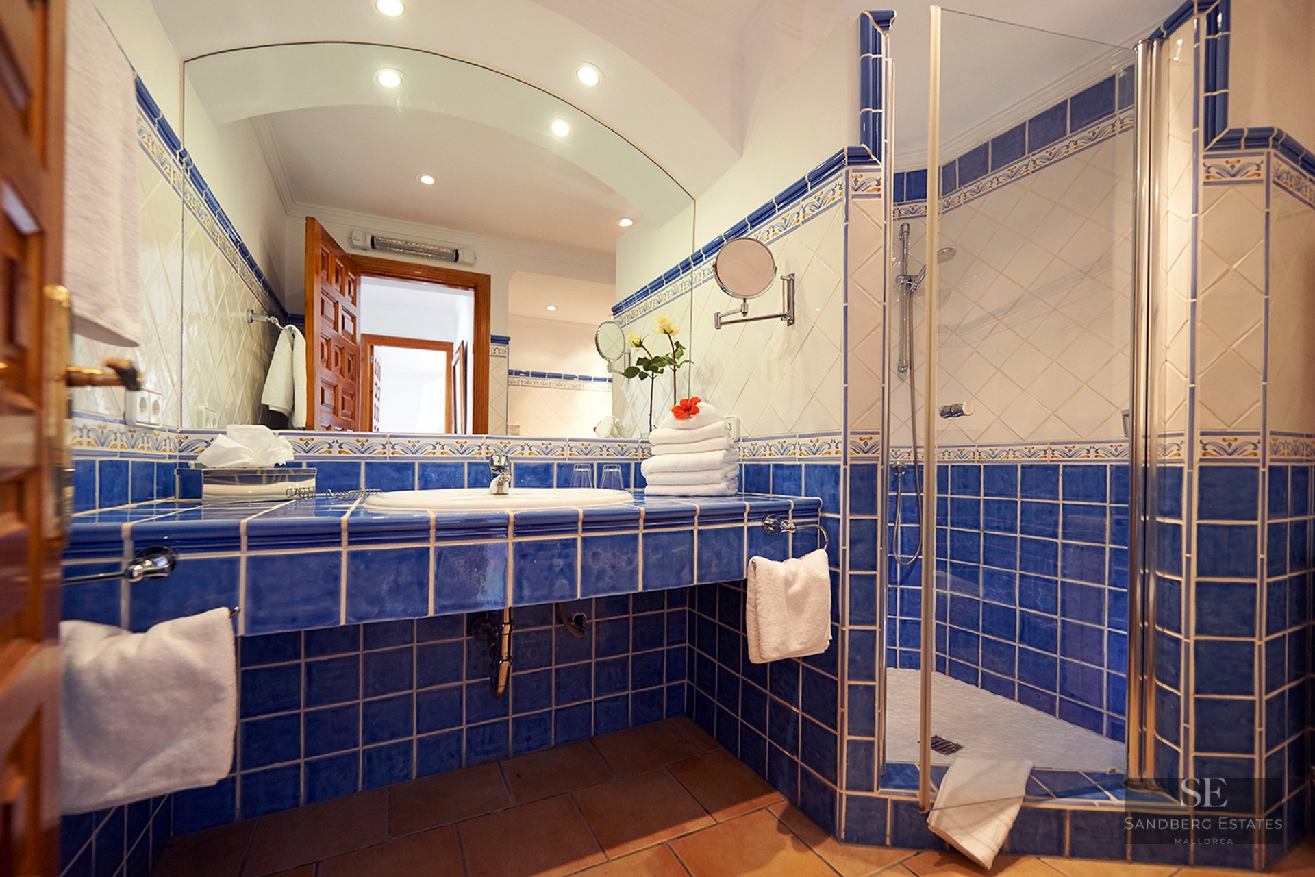 Blue and white tiled bathroom featuring a large arched mirror and a glass walk-in shower.