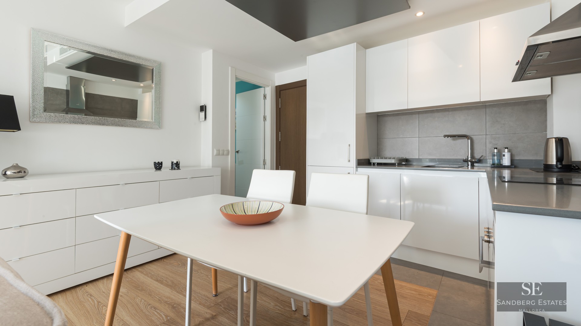 Cuisine moderne lumineuse avec des placards blancs, une crédence grise et une table à manger blanche.