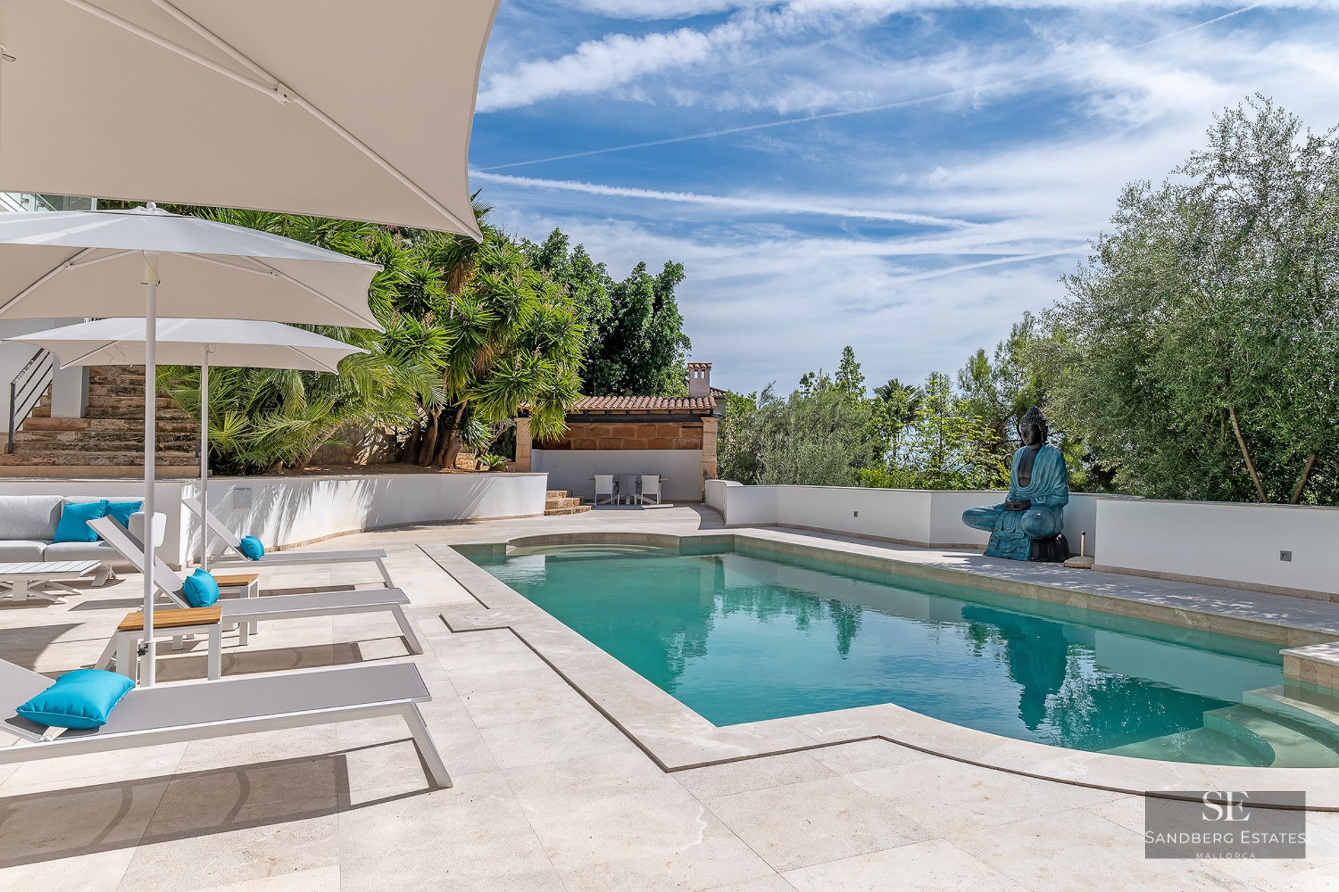 Modern turquoise swimming pool with grey sun loungers, white umbrellas, and a large blue Buddha statue.