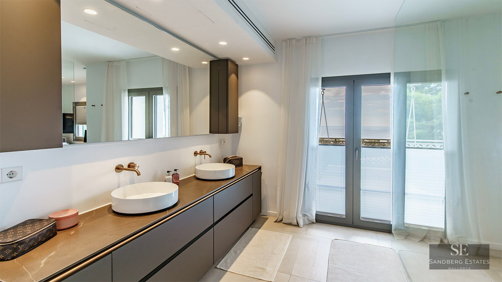Modern master bathroom featuring a double vanity with vessel sinks, large mirror, and balcony access with sea views.