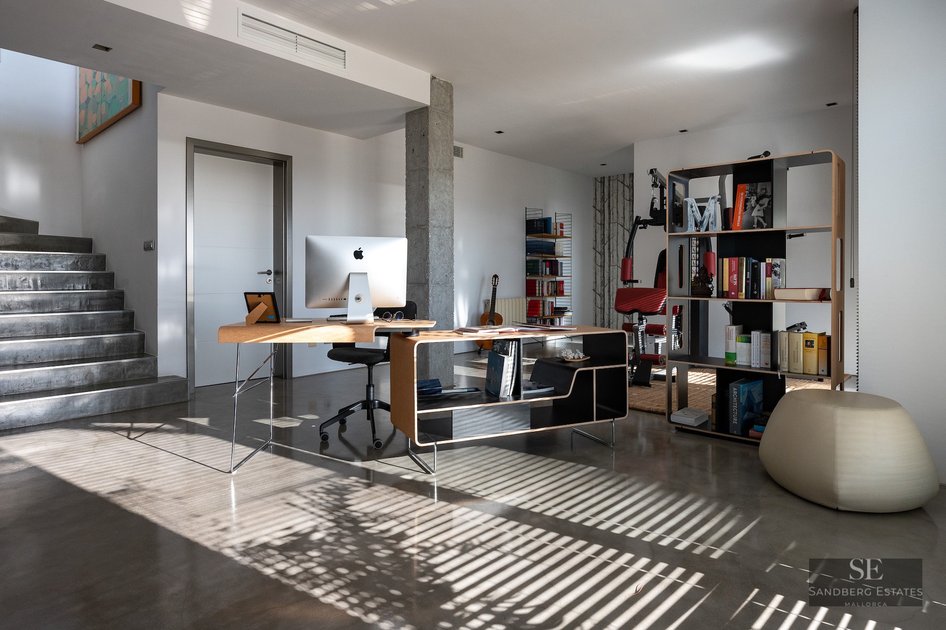 Bright home office featuring a designer wooden desk, iMac, polished concrete floors, and a bookshelf.