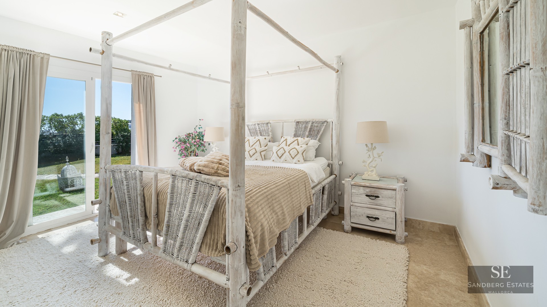 Bright bedroom featuring a white bamboo canopy bed, woven textures, and direct garden access via glass doors.