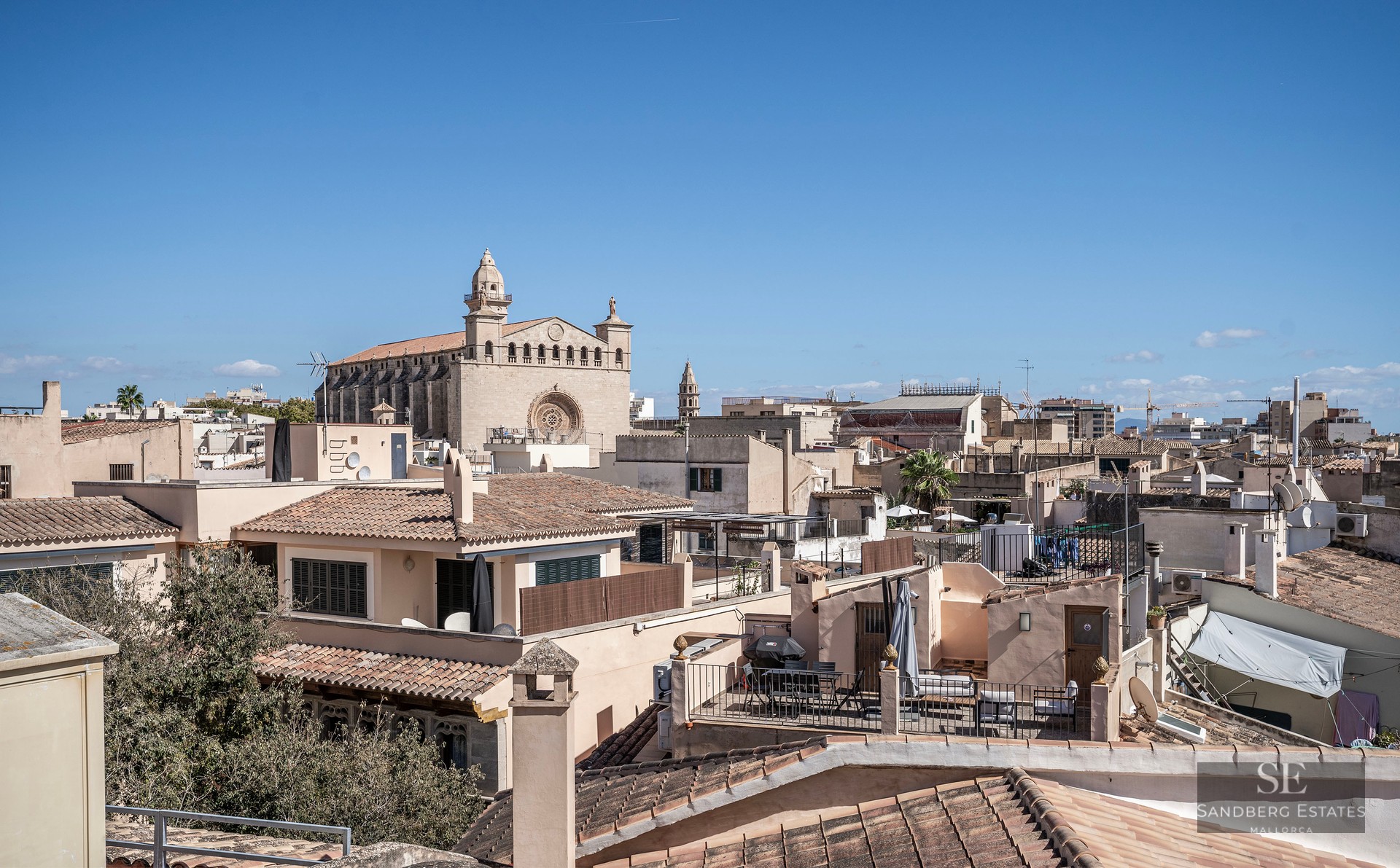 Vue surélevée de toits traditionnels en terre cuite et d'une majestueuse cathédrale en pierre sous un ciel bleu clair.