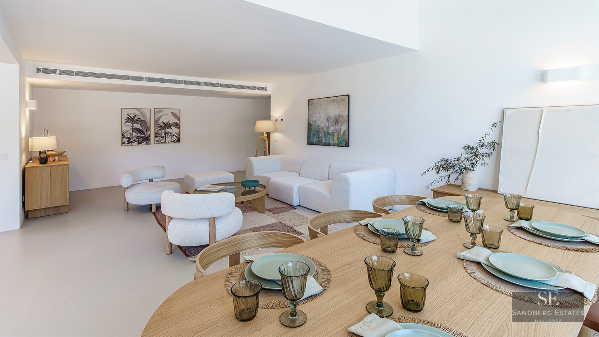 Spacious living and dining area featuring white bouclé sofas, a wooden dining table, and minimalist decor.