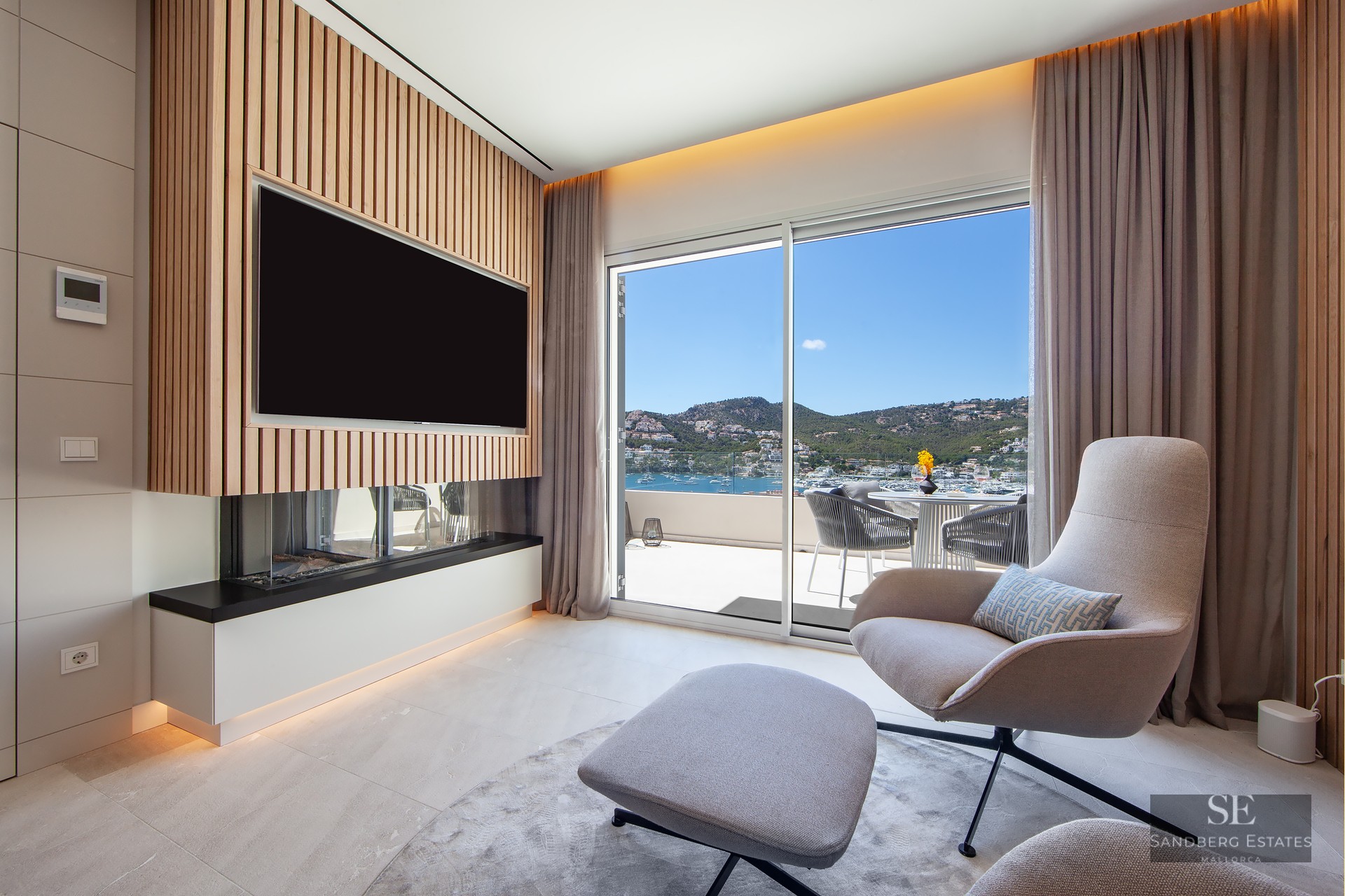 Contemporary lounge featuring an armchair, fireplace, wood-slat TV wall, and panoramic harbor views through sliding doors.