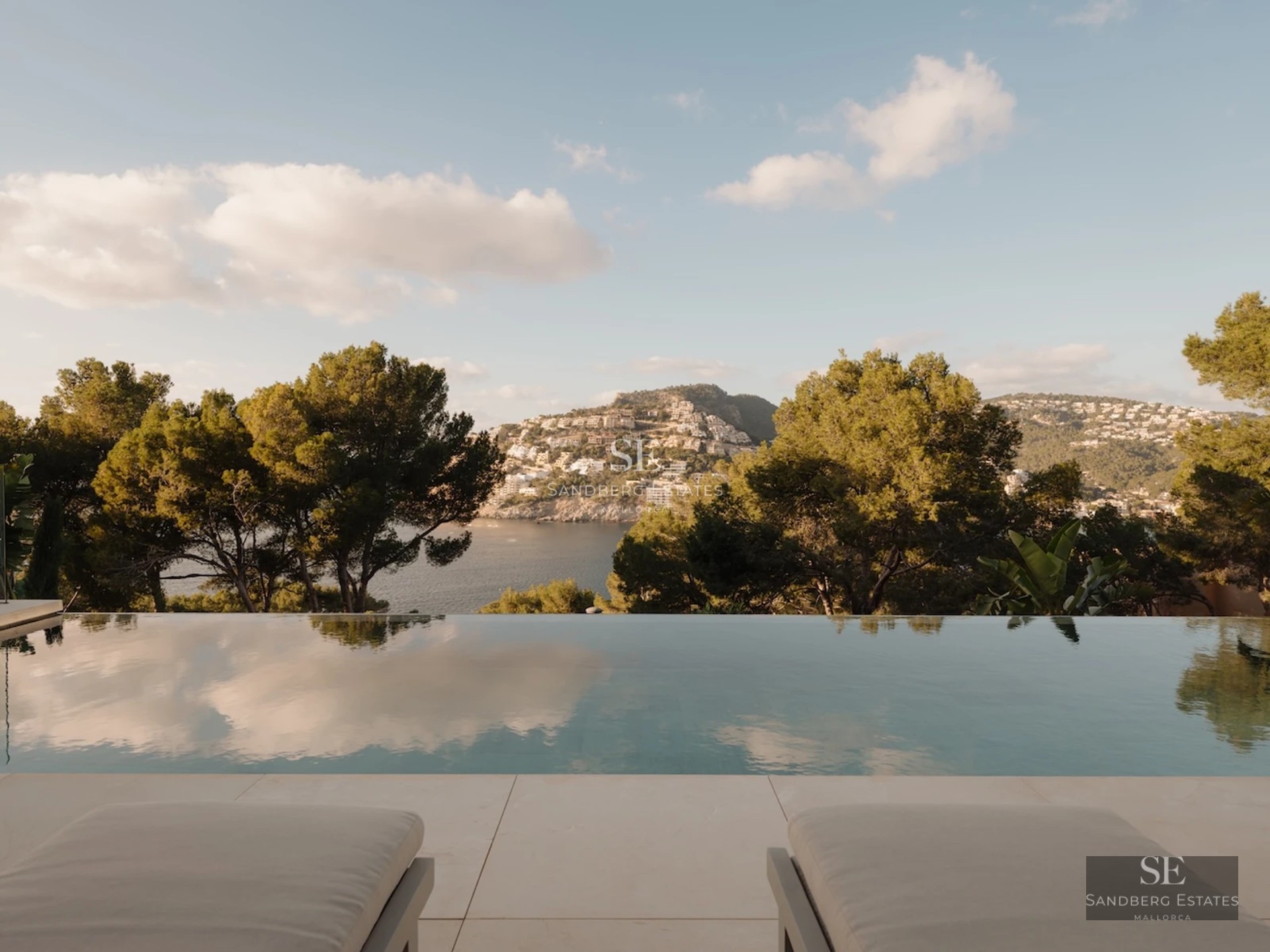 Spacious living room with large windows, light wood floors, a modern fireplace, and views of the garden with a pool. Minimalist and bright design.