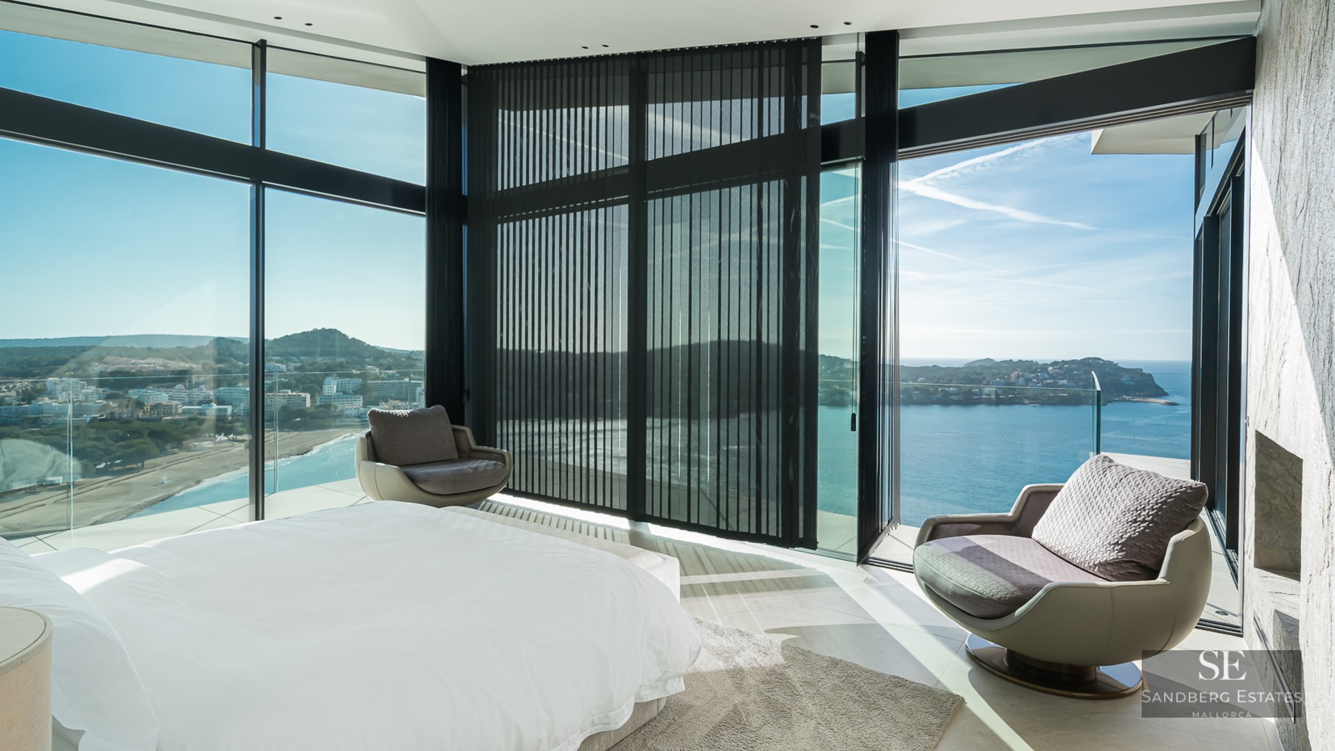 Modern bedroom with floor-to-ceiling windows offering a panoramic sea view and designer swivel chairs.