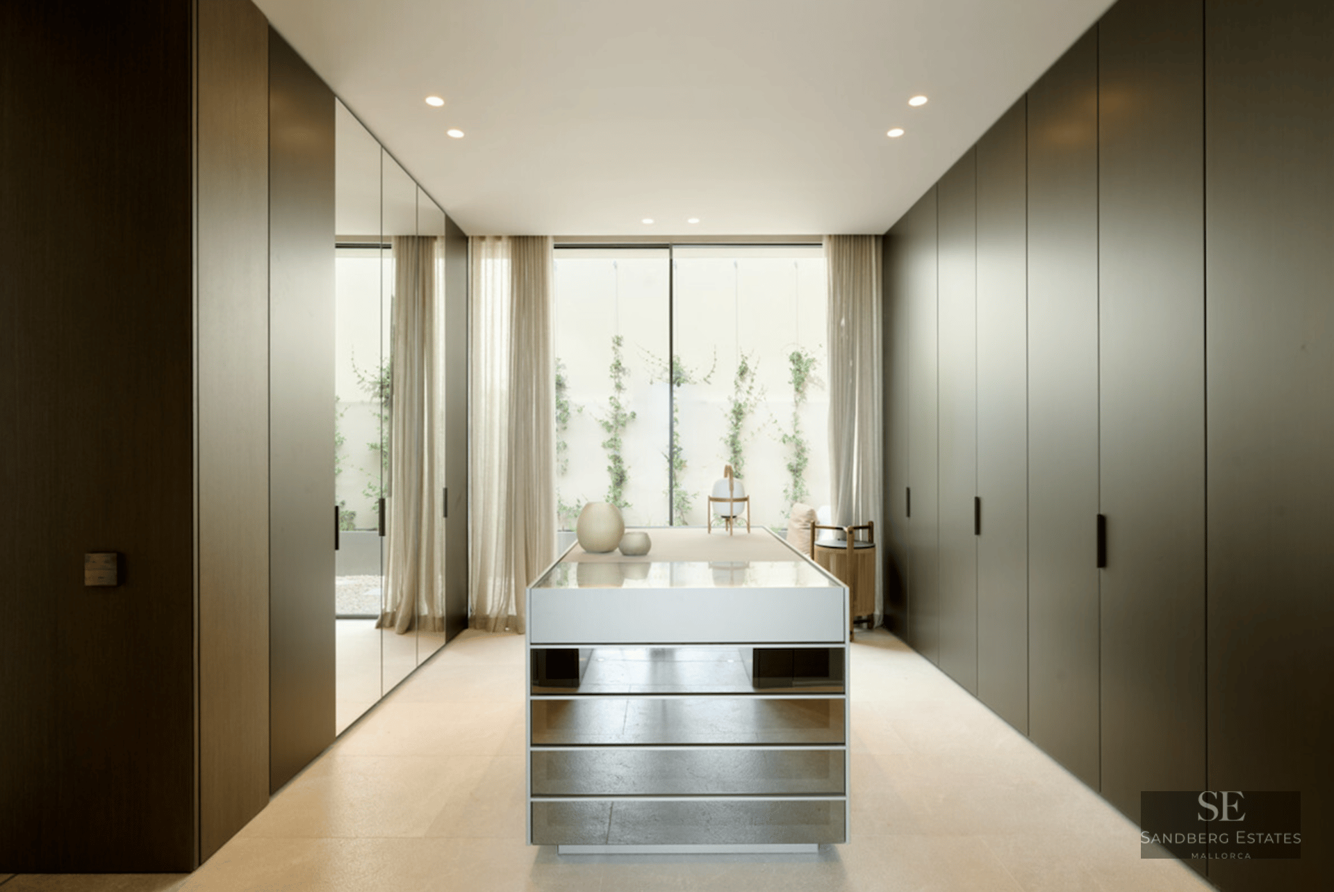 Modern walk-in closet with dark floor-to-ceiling cabinets, a mirrored island, and a garden window.