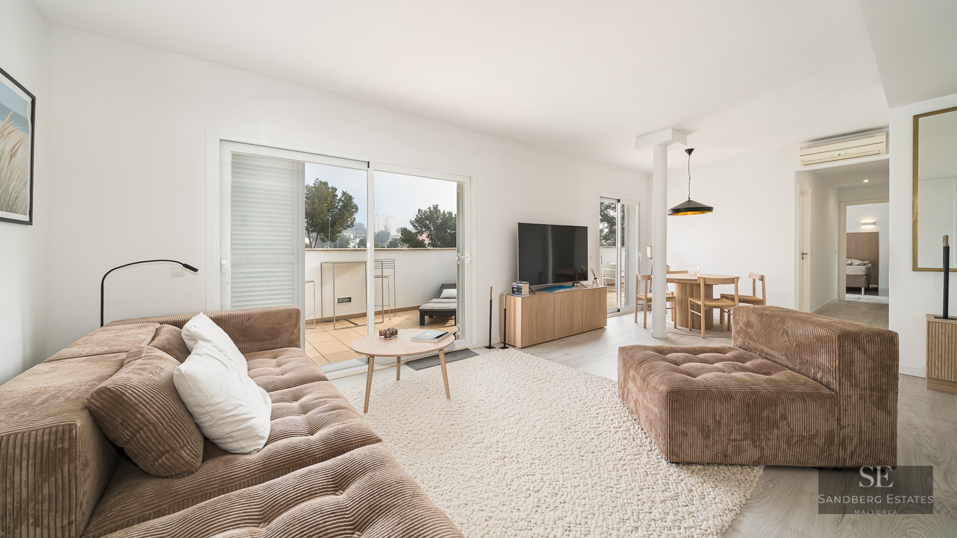 Modern living room with a brown corduroy sofa, large rug, and sliding glass doors leading to a sunlit terrace.