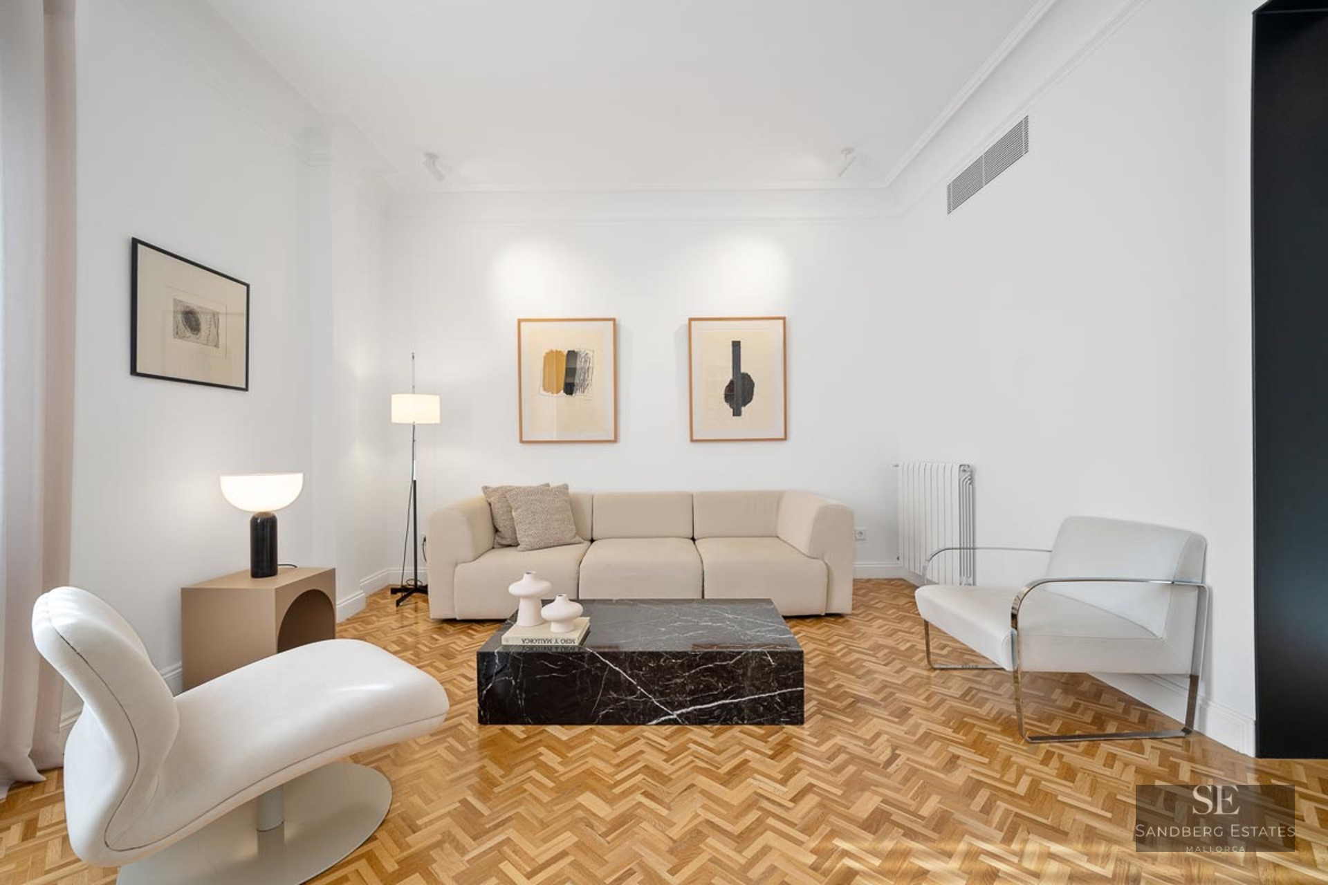 Bright living room with white walls, herringbone wood floor, beige sofa, and a striking black marble coffee table.
