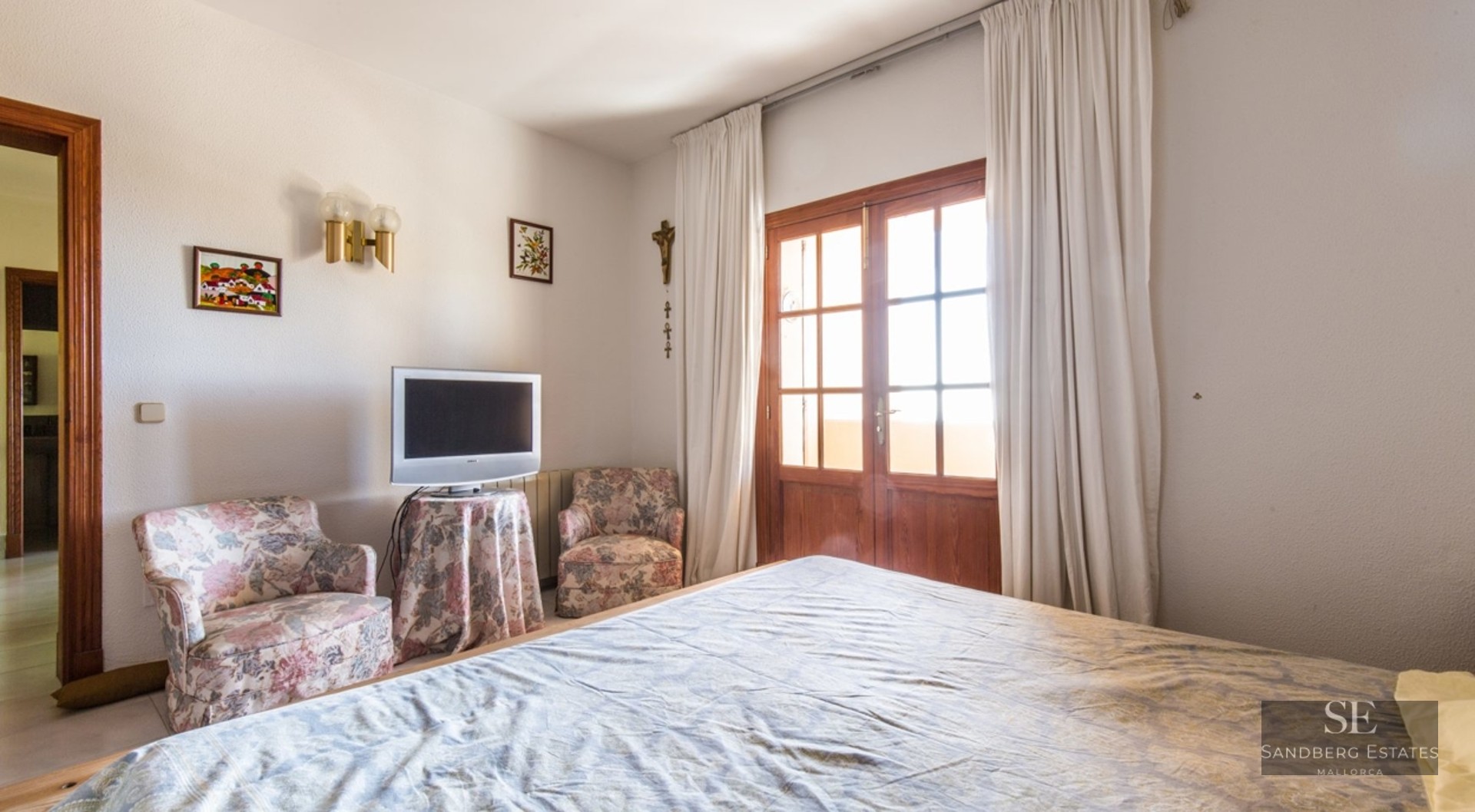 Bedroom featuring a bed, two floral armchairs, and wooden French doors leading to a balcony.