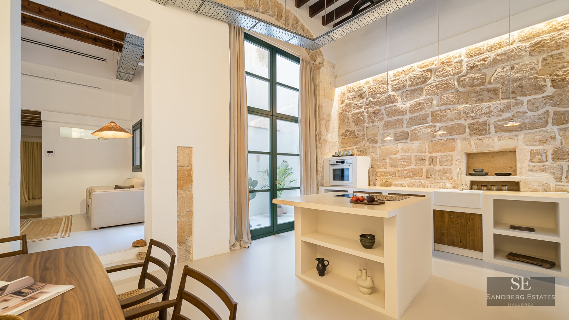 Minimalist kitchen featuring a large natural stone wall, white island, and high ceilings with wooden beams.