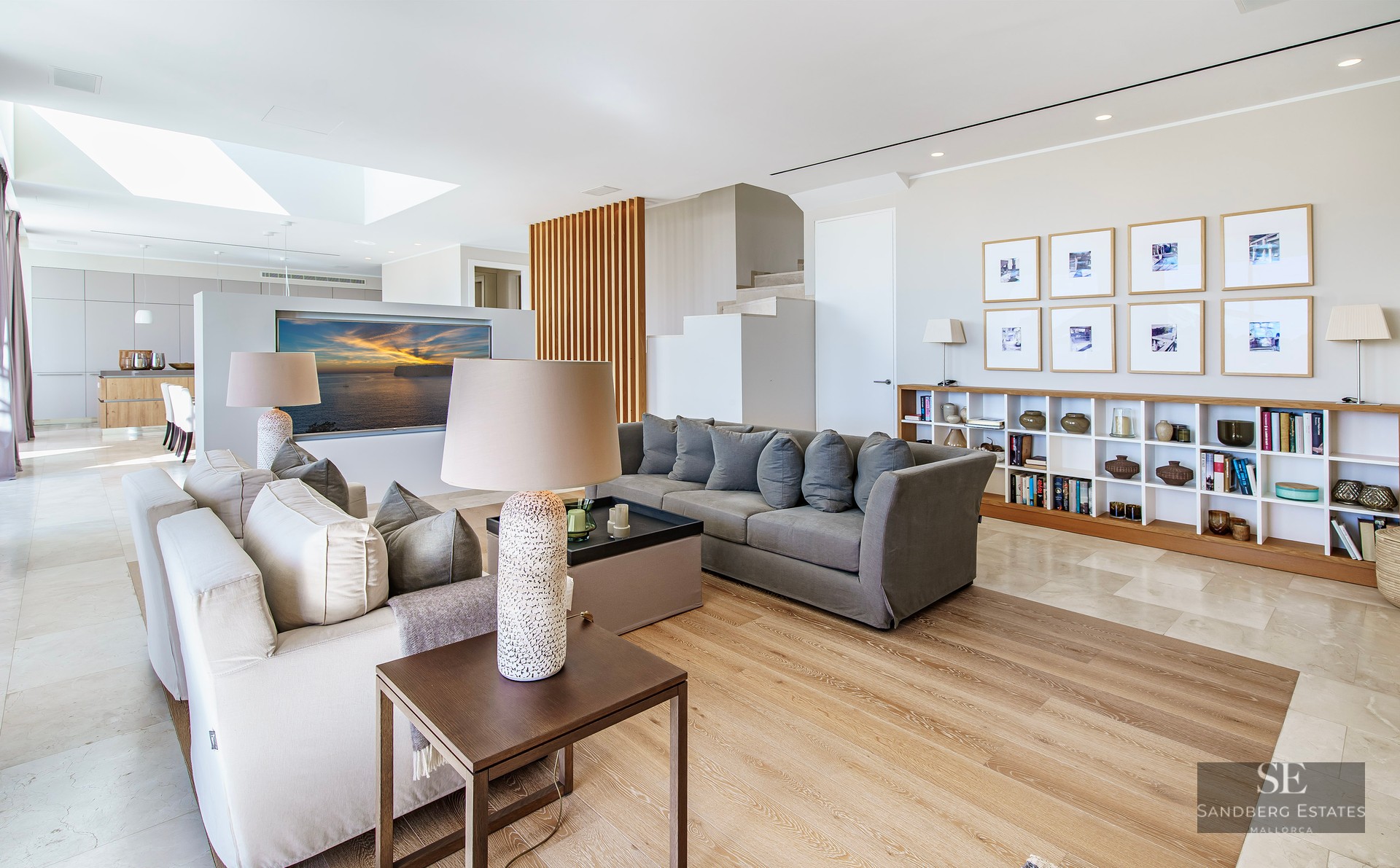Spacious modern living room with grey sofas, light wood floors, a skylight, and a decorative wooden slat wall.