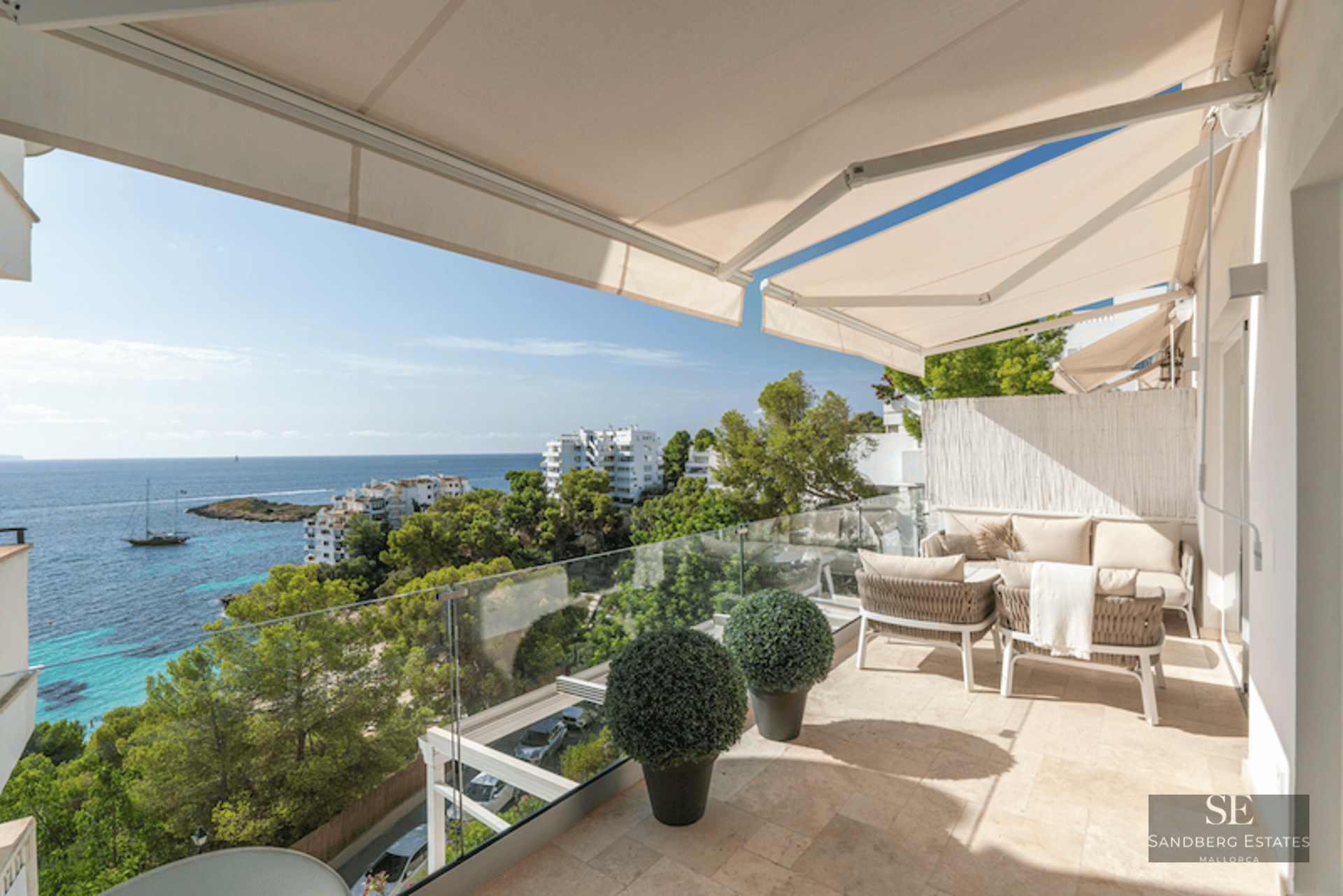 Modern terrace with beige sofas, glass railings, and panoramic Mediterranean sea views under retractable awnings.