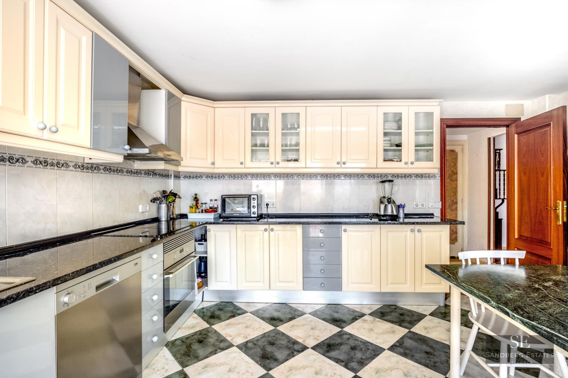 Bright kitchen with cream cabinets, dark granite countertops, and a green and white checkered tiled floor.