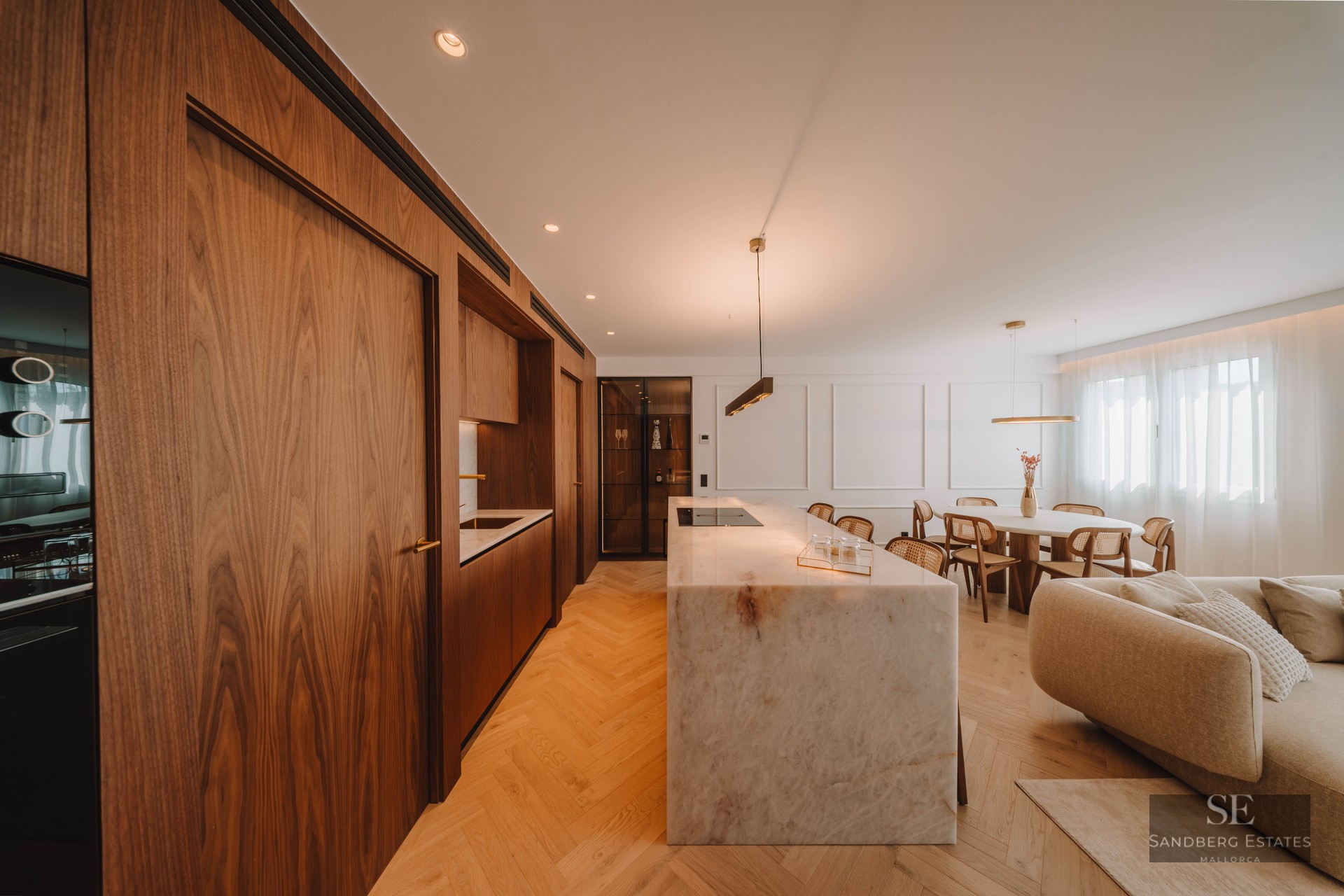 Modern open-plan kitchen featuring a large marble island, walnut cabinetry, and herringbone wood floors.