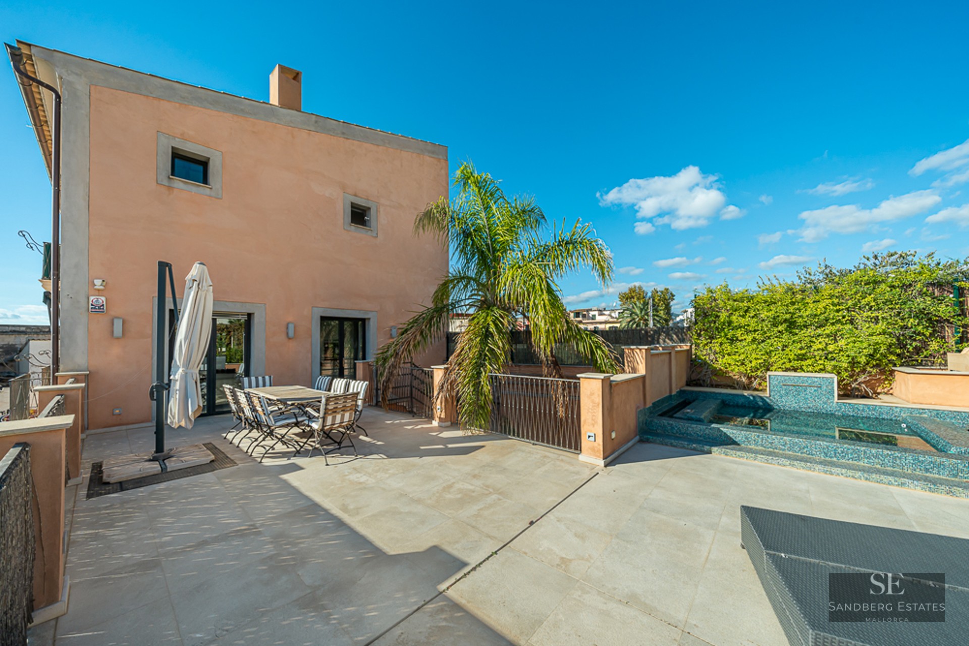 Mediterranean terrace with stone tile flooring, outdoor dining set, a palm tree, and a small tiled plunge pool under a clear blue sky.